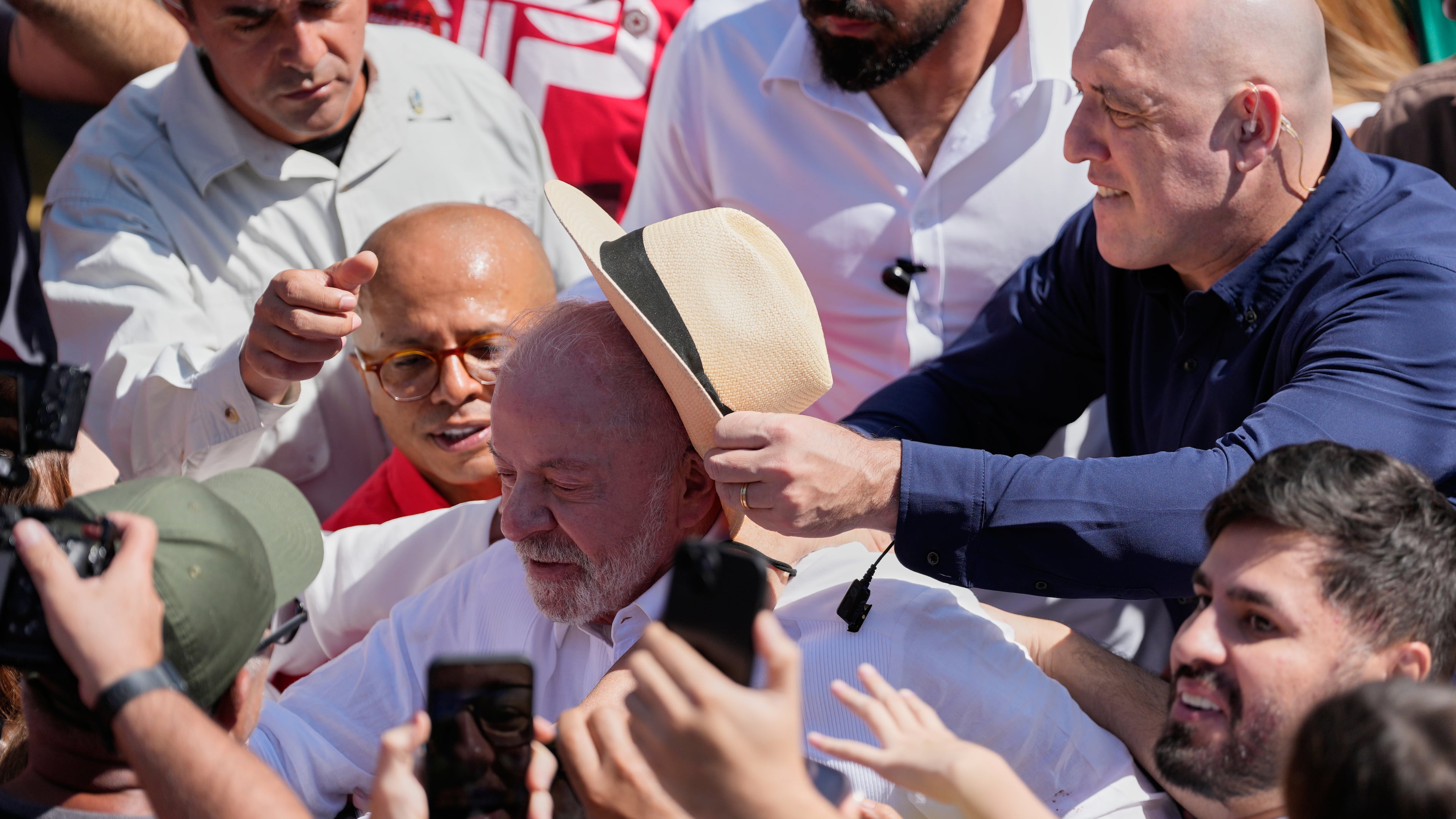 A security officer places a hat on President Luiz Inacio Lula da Silva as he leaves after voting during general elections amid a crowd in Sao Bernardo do Campo, Brazil, Sunday, Oct. 4, 2026. (AP Photo/Andre Penner)