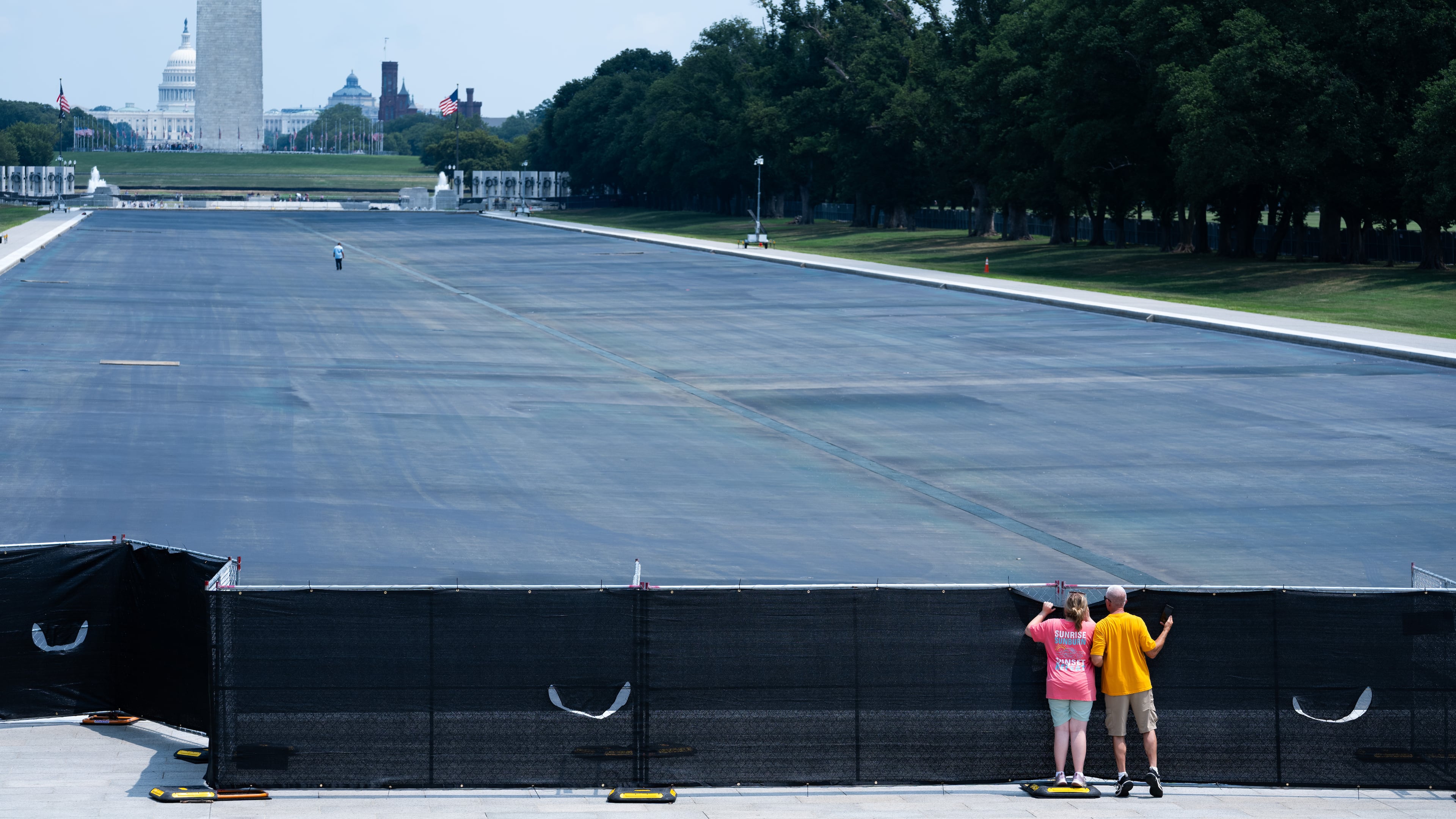 Individuals peek over the fence to see the drained Lincoln Memorial Reflecting Pool,, Monday, July 27, 2026, in Washington. (AP Photo/Allison Robbert)