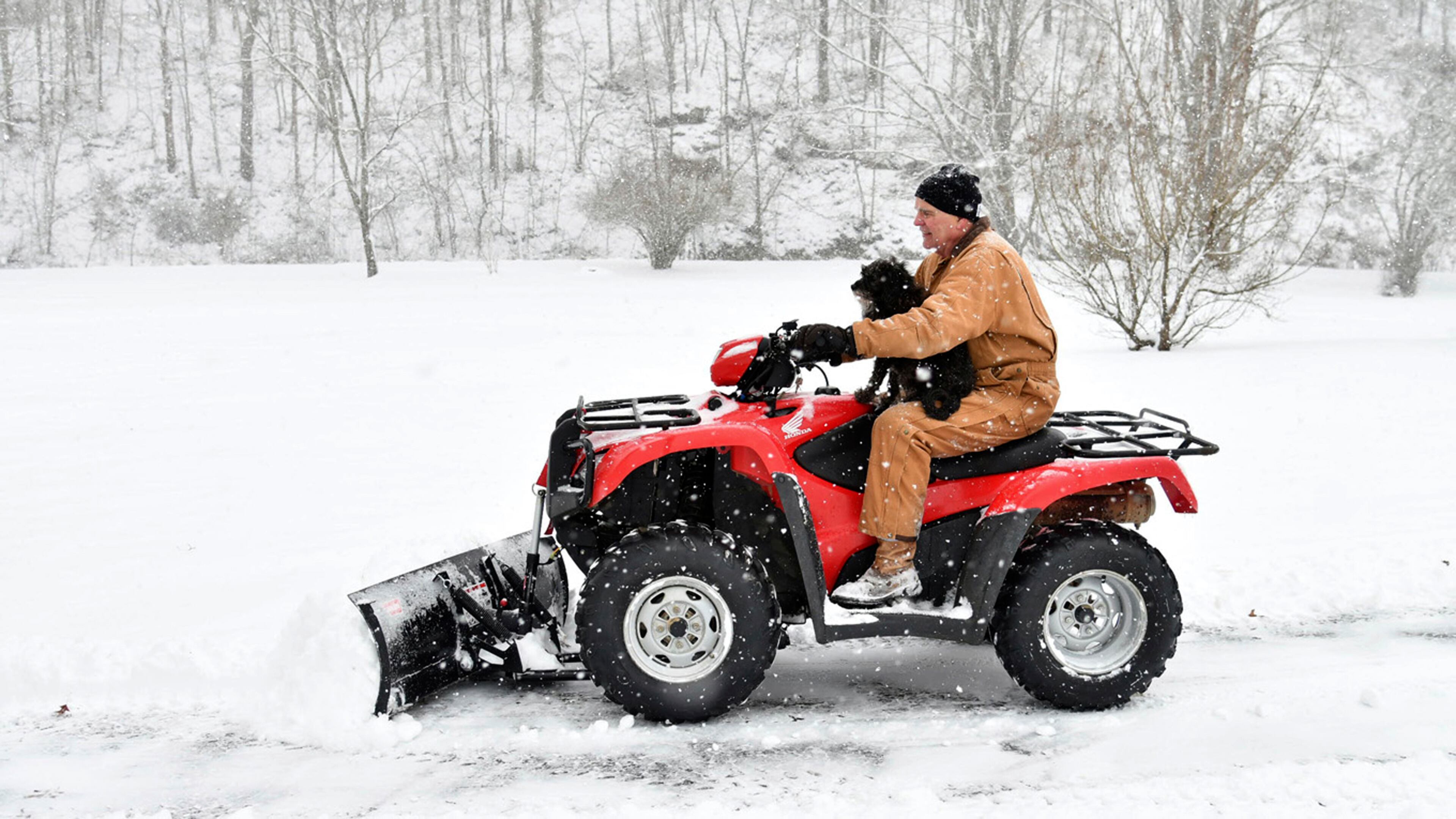 Rick Keelin clears a driveway while riding with his four-wheeler with his dog Nicole, Tuesday, Jan. 16, 2018, as snow continues to accumulate in Catlettsburg, Ky. (Kevin Goldy/The Daily Independent via AP)