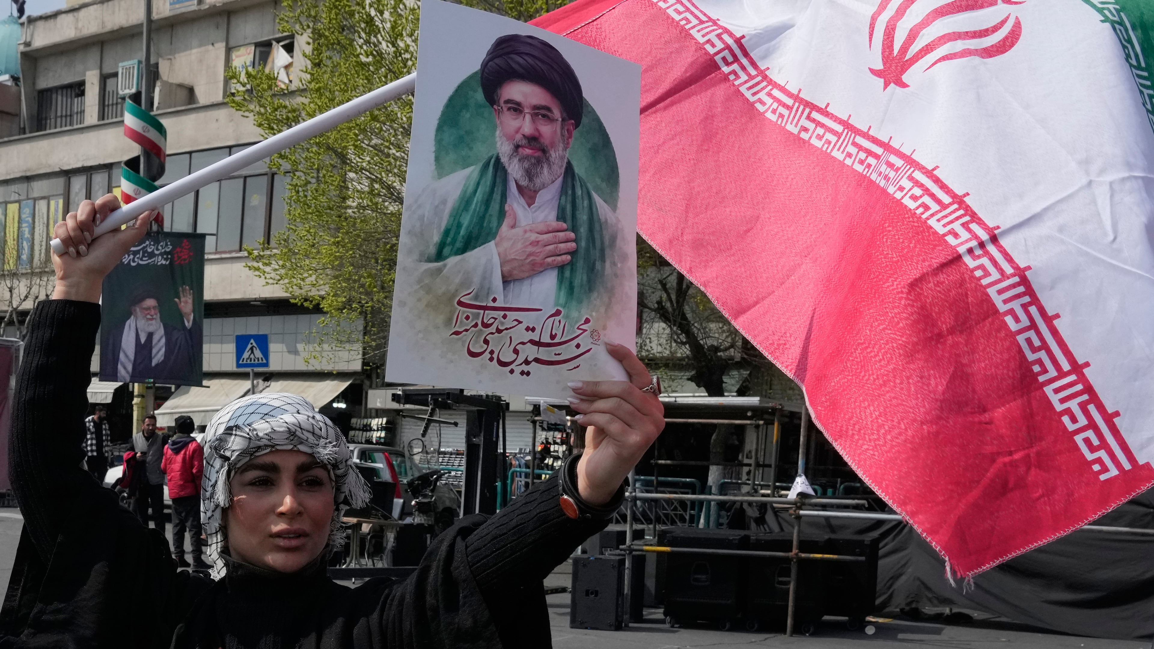 A woman displays a poster of the Iranian Supreme Leader Ayatollah Mojtaba Khamenei as she waves her country's flag during a campaign in support of the government at the Enqelab-e-Eslami, or Islamic Revolution, square in downtown Tehran, Iran, Saturday, March 14, 2026. (AP Photo/Vahid Salemi)