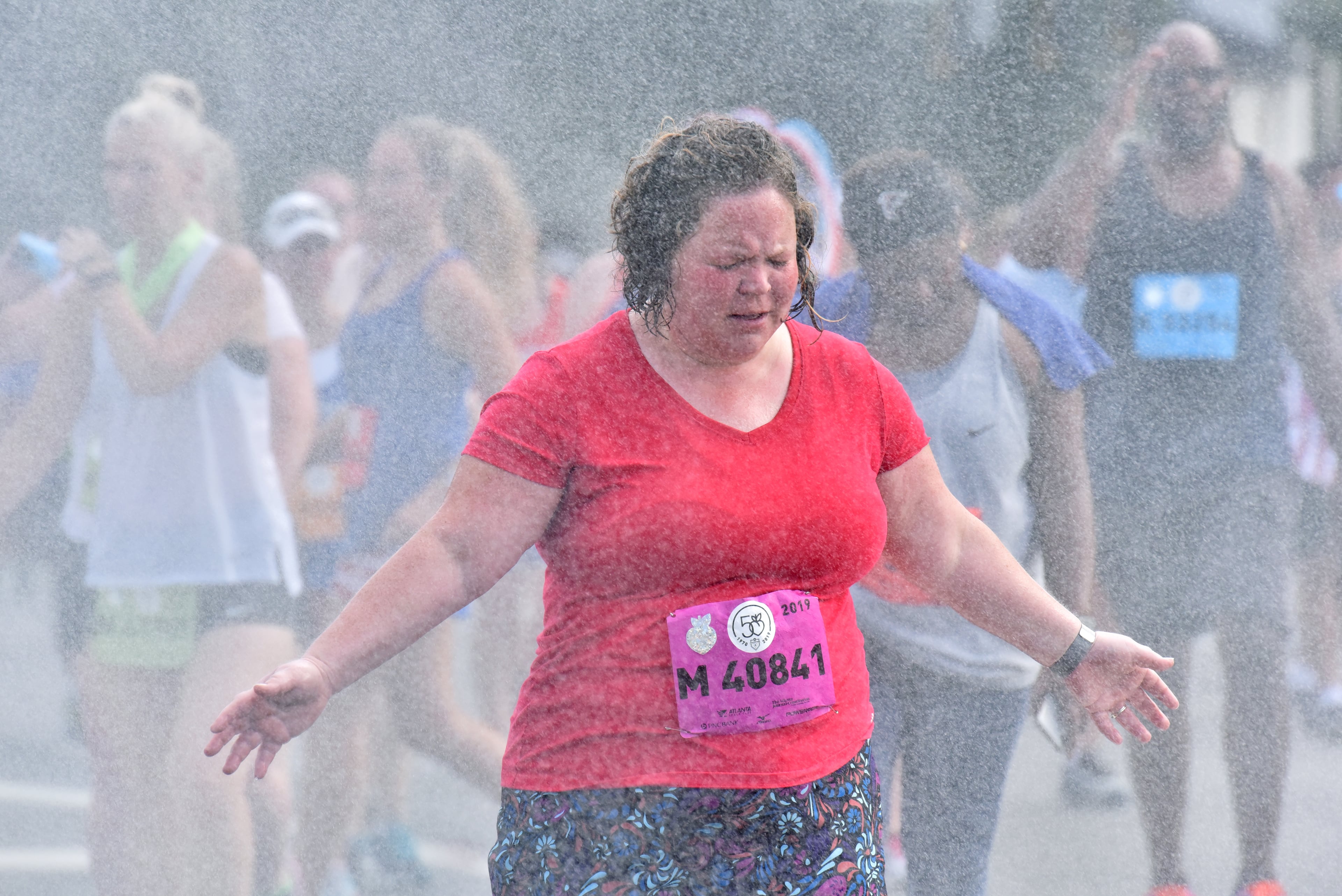 A runner cools off with mist as she makes her way down Peachtree Road during the 50th AJC Peachtree Road Race on Thursday, July 4, 2019. (Hyosub Shin / Hyosub.Shin@ajc.com)
