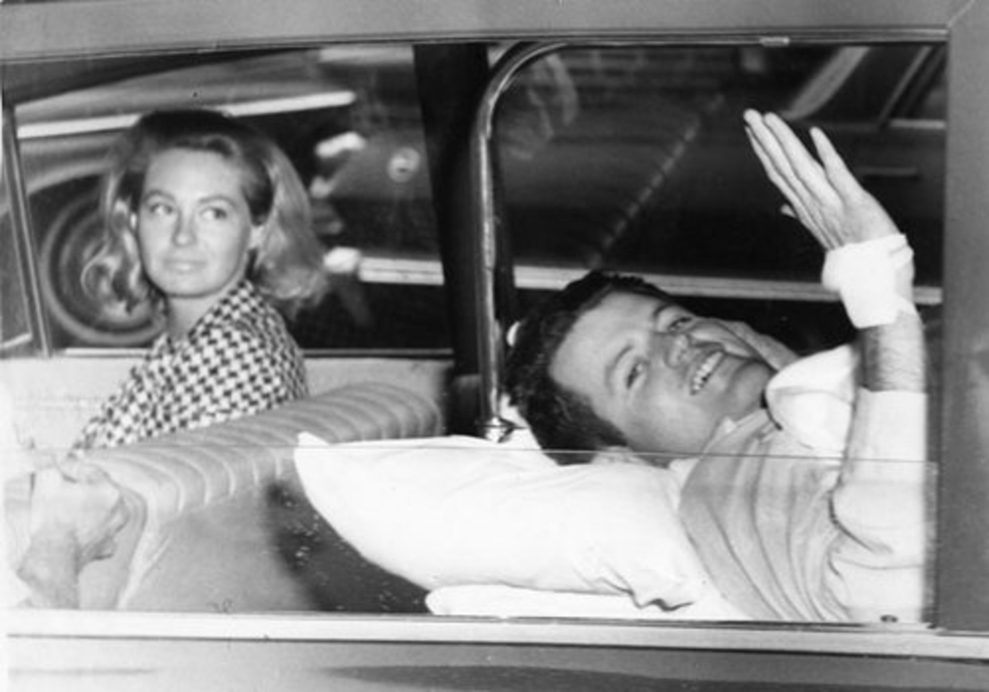 Sen. Edward Kennedy waves from the back of an ambulance as he leaves a Boston hospital after undergoing treatment following an airplane crash in 1964. In the front seat is his first wife, Joan Kennedy.