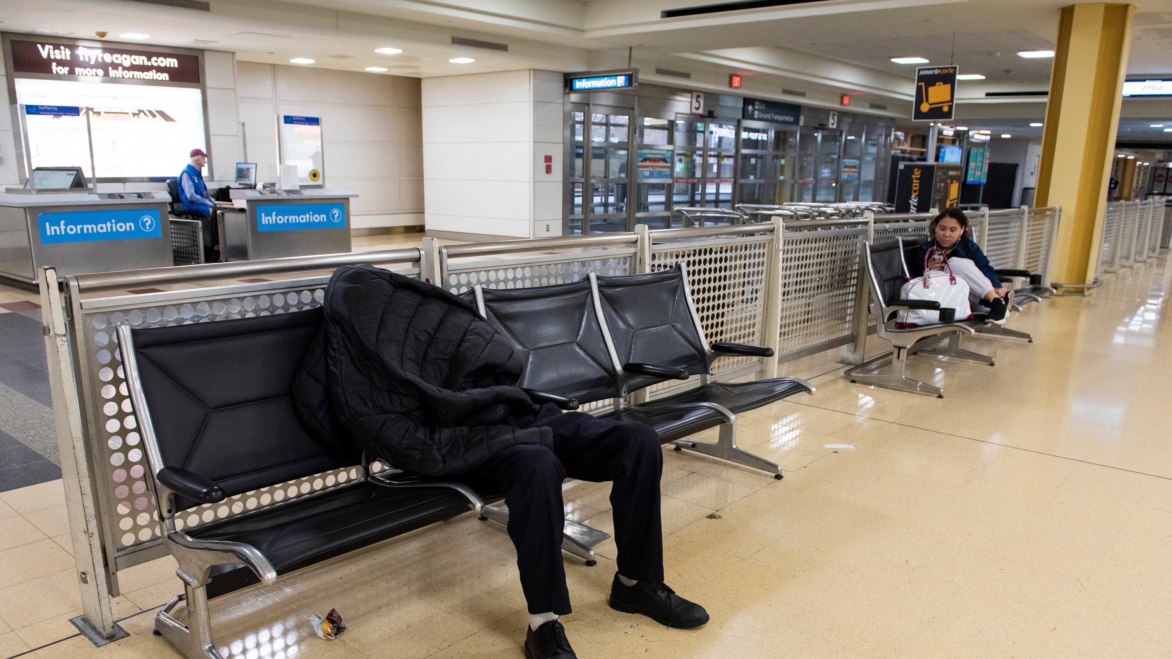 A man sleeps in the baggage claim area of Ronald Reagan National Airport, in Arlington, Va., Monday, March 16, 2026. (AP Photo/Cliff Owen)