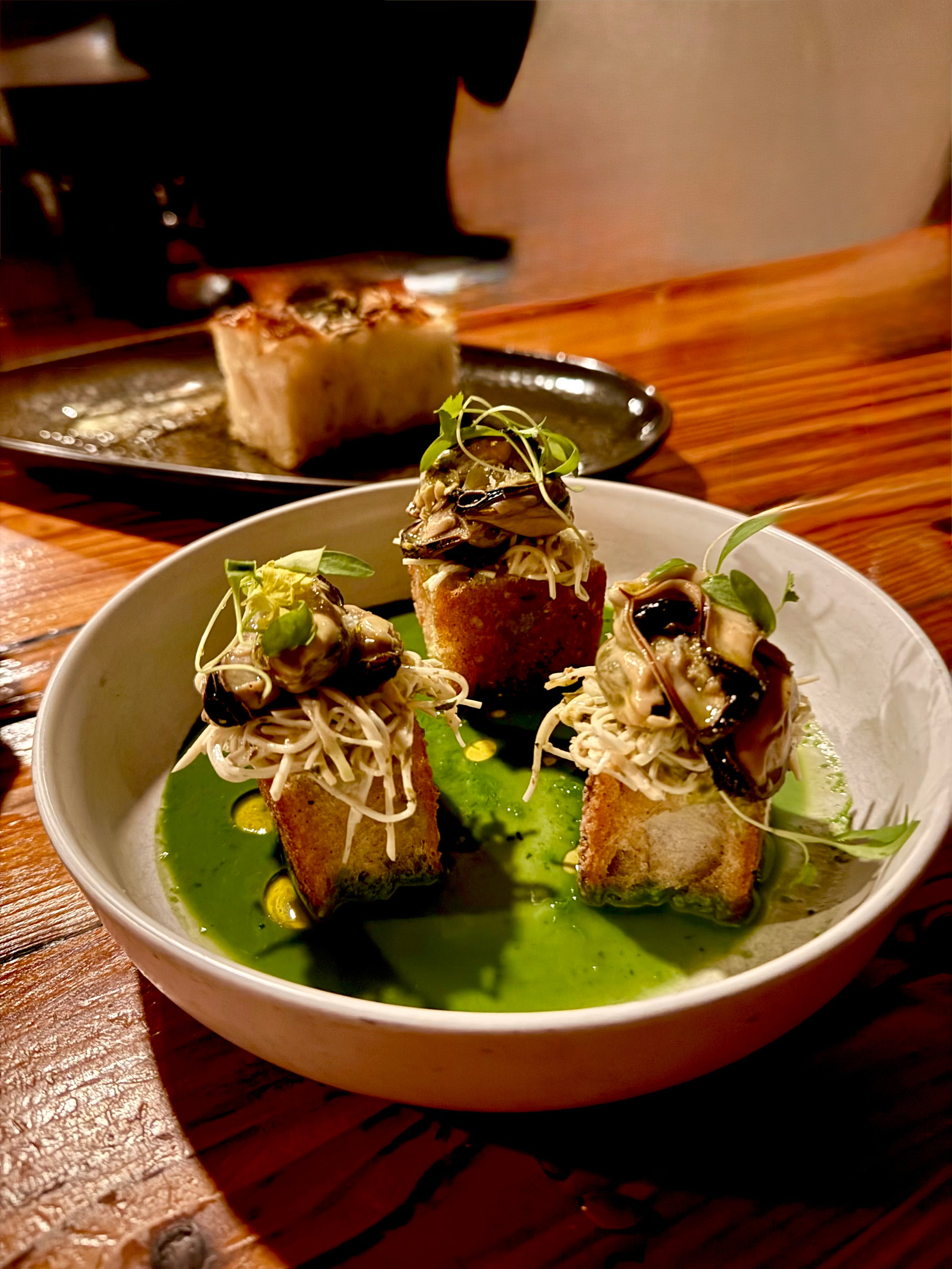 The Marinated Mussels at BoccaLupo rest atop thick-cut French croutons, crisped in butter to a deep, resonant gold with a sprinkling of Parmesan cheese and fronds of micro cilantro. (Angela Hansberger for the AJC)