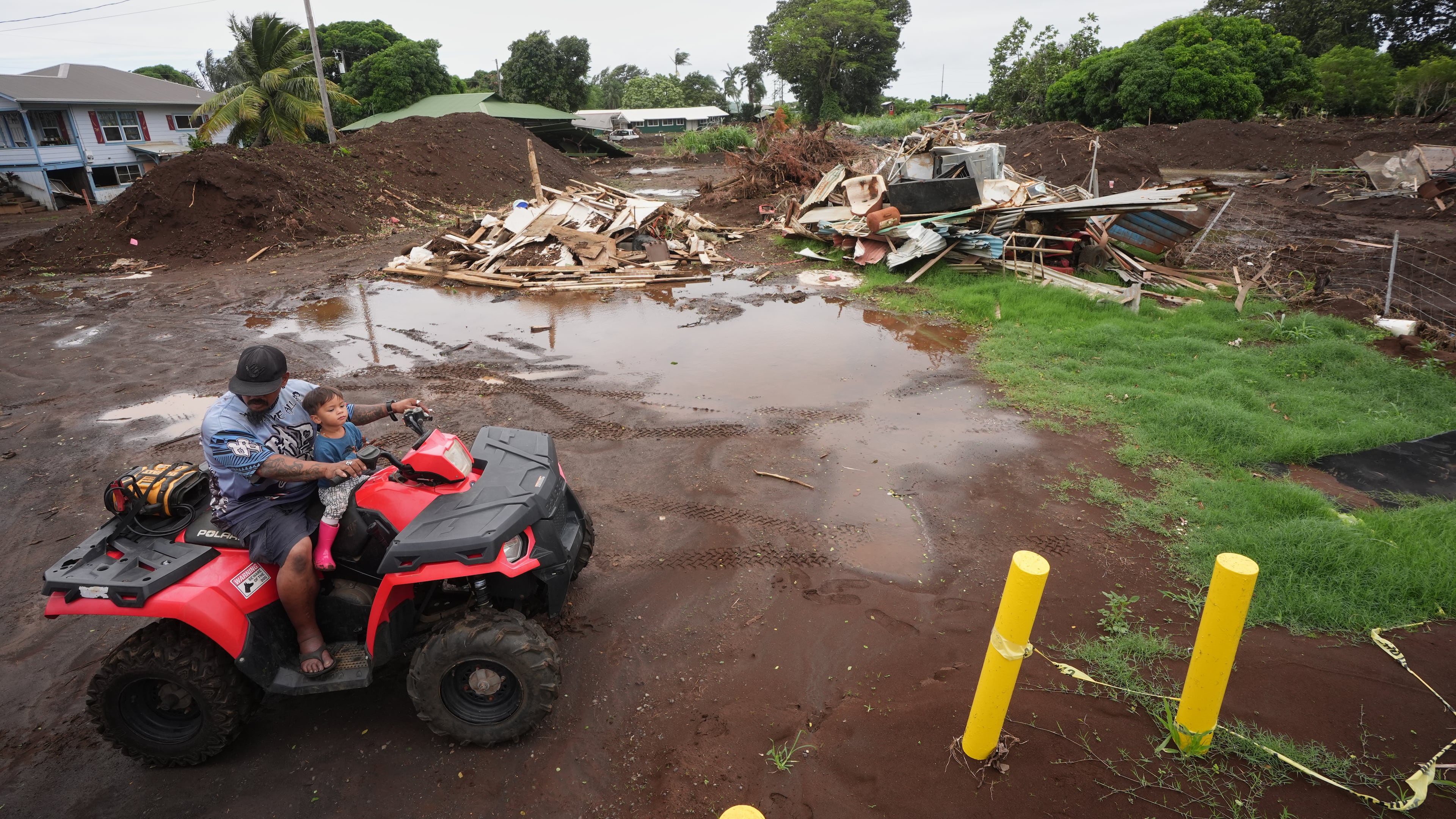 A man rides with his son near where a home was destroyed during last month's Hurricane Lala, as floodwaters from Hurricane Nolo recedes Sunday, Sept. 27, 2026, in Naalehu, Hawaii. (AP Photo/Gregory Bull)