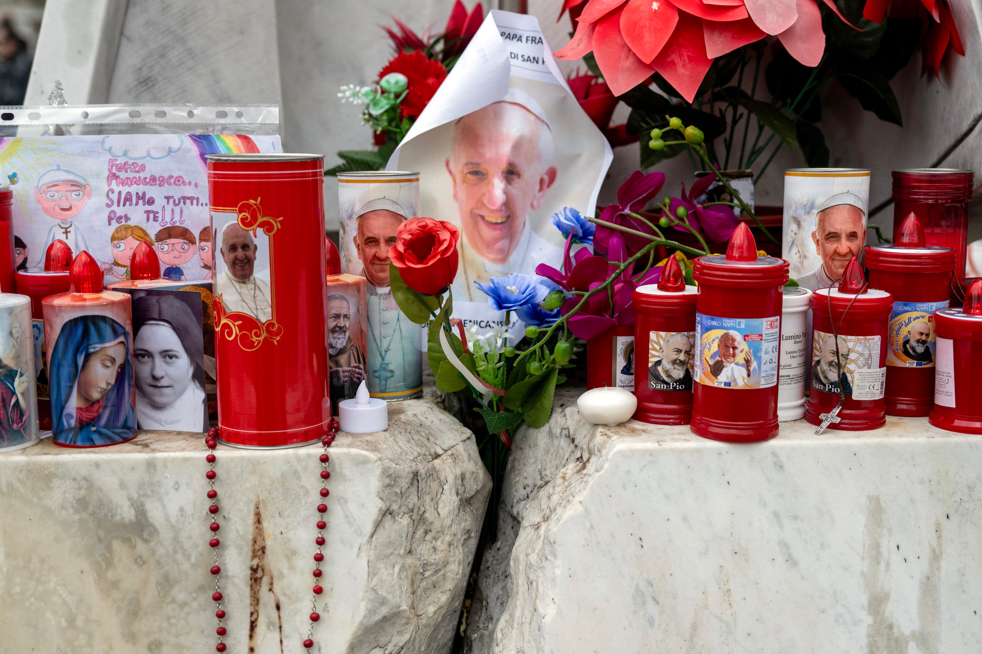 Flowers and candles are placed at the base of the statue of Pope John Paul II on Monday, Feb. 24, 2025, outside Gemelli Hospital in Rome, where Pope Francis was being treated for pneumonia, a complex infection and kidney problems. (James Hill / The New York Times)
