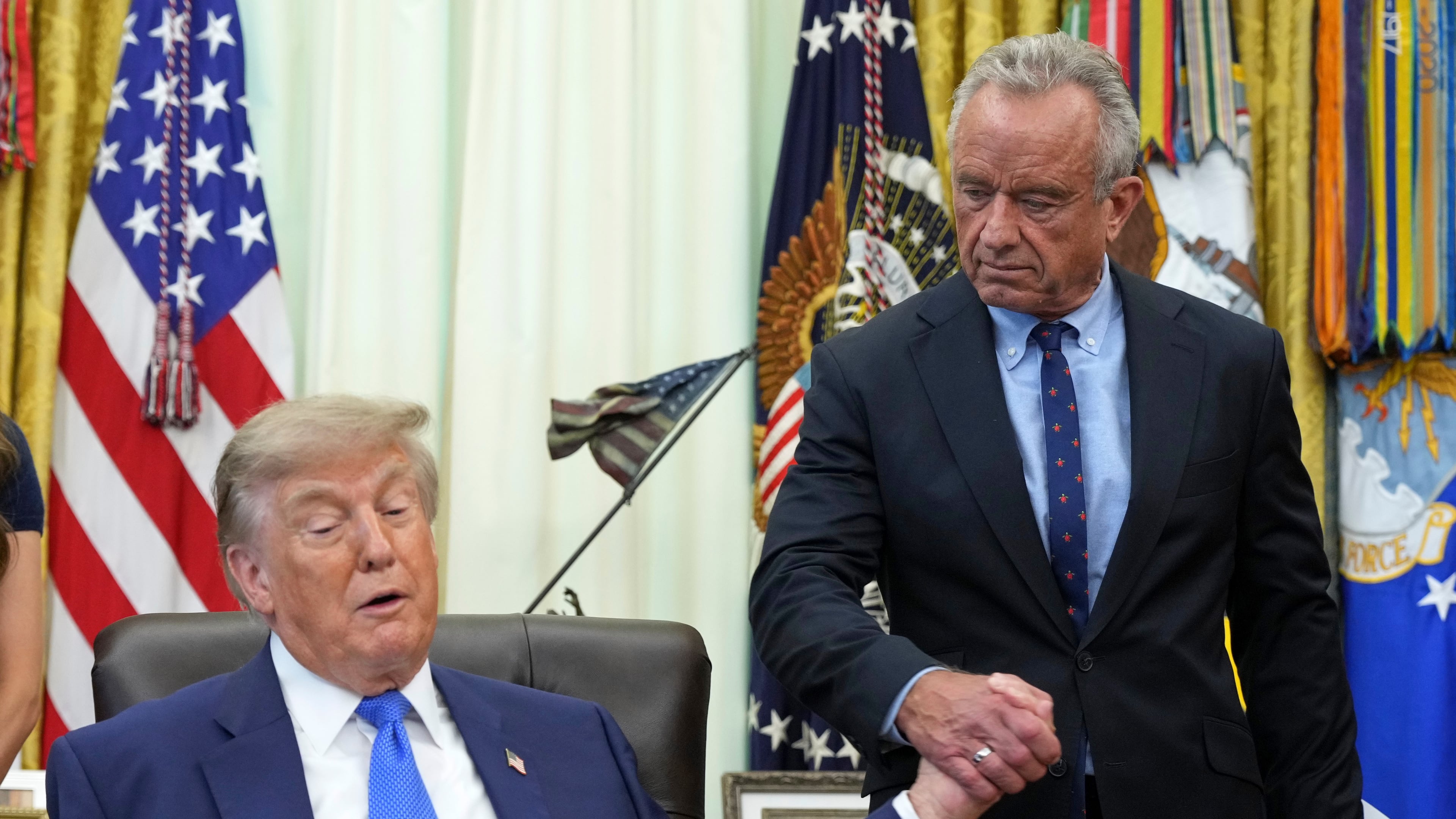 President Donald Trump, left, shakes the hand of Health and Human Services Secretary Robert F. Kennedy Jr. during a meeting to sign an executive order about vaccines, Monday, Aug. 10, 2026, in the Oval Office of the White House in Washington. (AP Photo/Jacquelyn Martin)