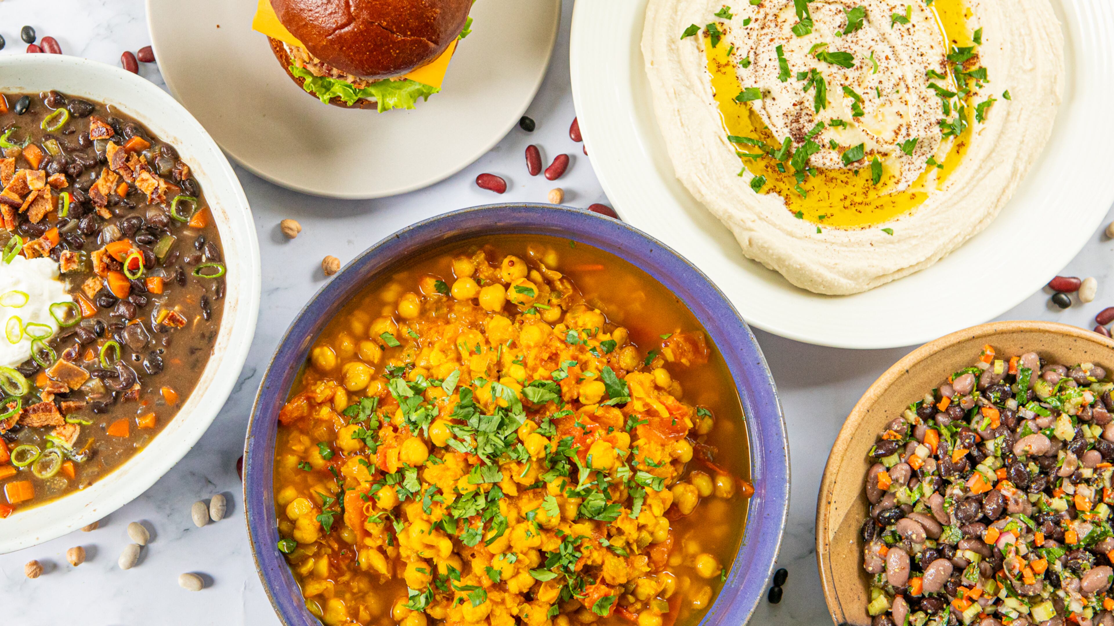Beans deliver interesting, affordable dishes to your table. (Clockwise from top left:) bean burger, Any Bean Hummus, Mustardy Bean Salad, chana masala and black bean soup. (Aaliyah Man for the AJC/food styling by Kate Williams)