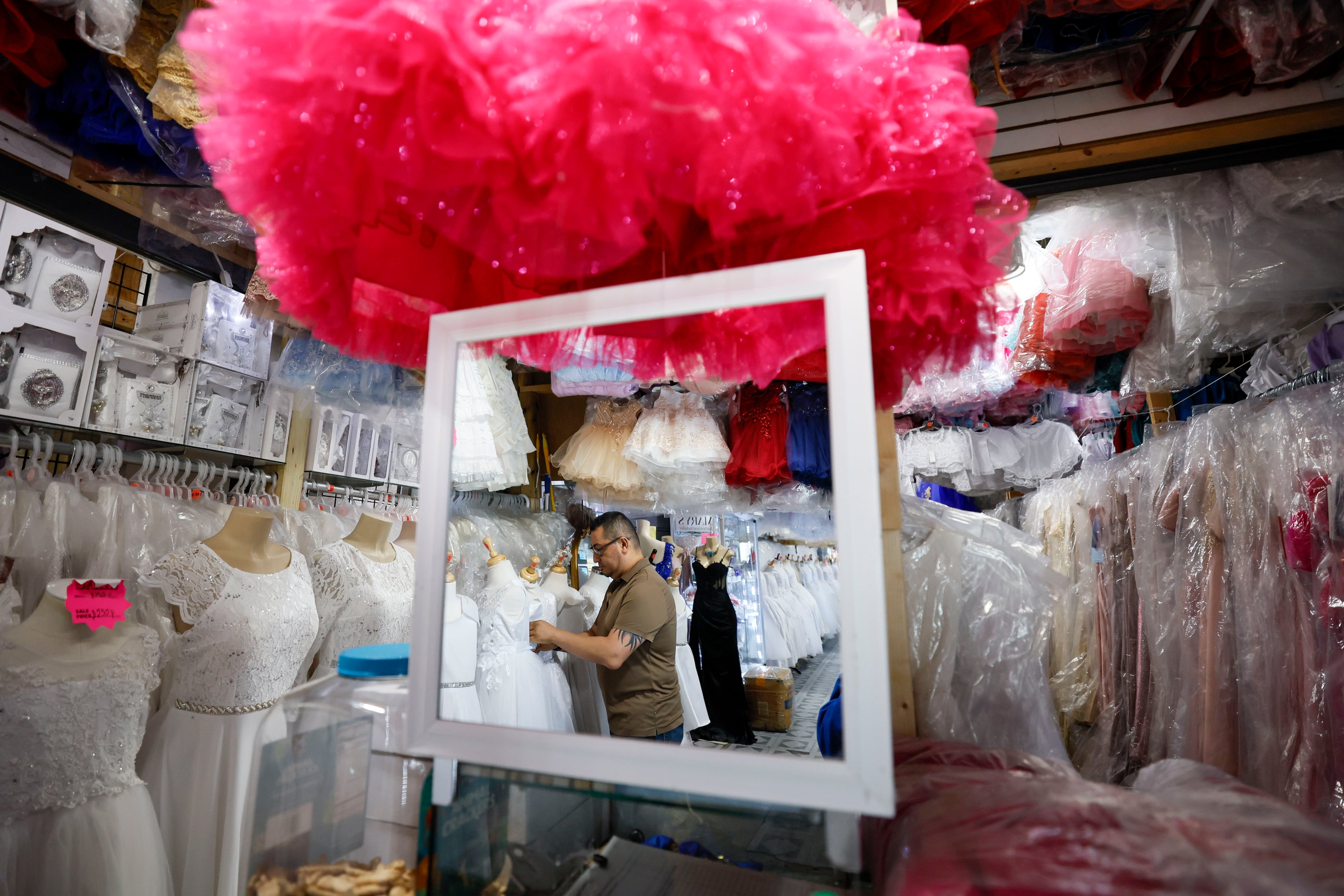 Frank Chavez, owner of Lizzy Fashion, arranges dresses at his shop in Plaza Fiesta. He anticipates his sales are down by 30-40% year-over-year. (Miguel Martinez/ AJC)