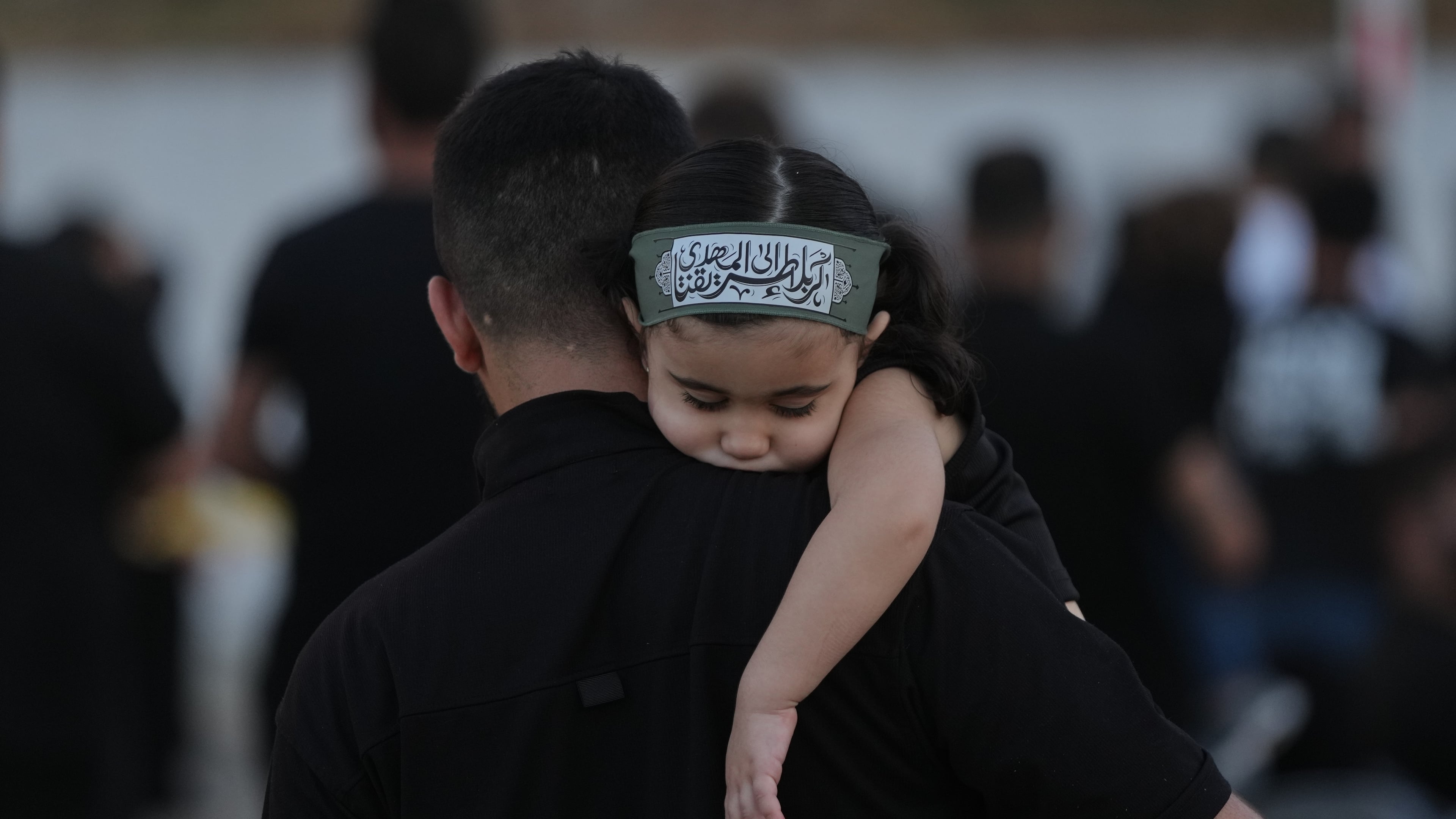 A girl wearing an Ashoura headband rests on her father's shoulder during a sermon marking the third day of Ashoura, the Shiite Muslim commemoration of the 7th-century death of Imam Hussein, the grandson of the Prophet Muhammad, in the southern port city of Tyre, Lebanon, Friday, June 19, 2026. (AP Photo/Hassan Ammar)