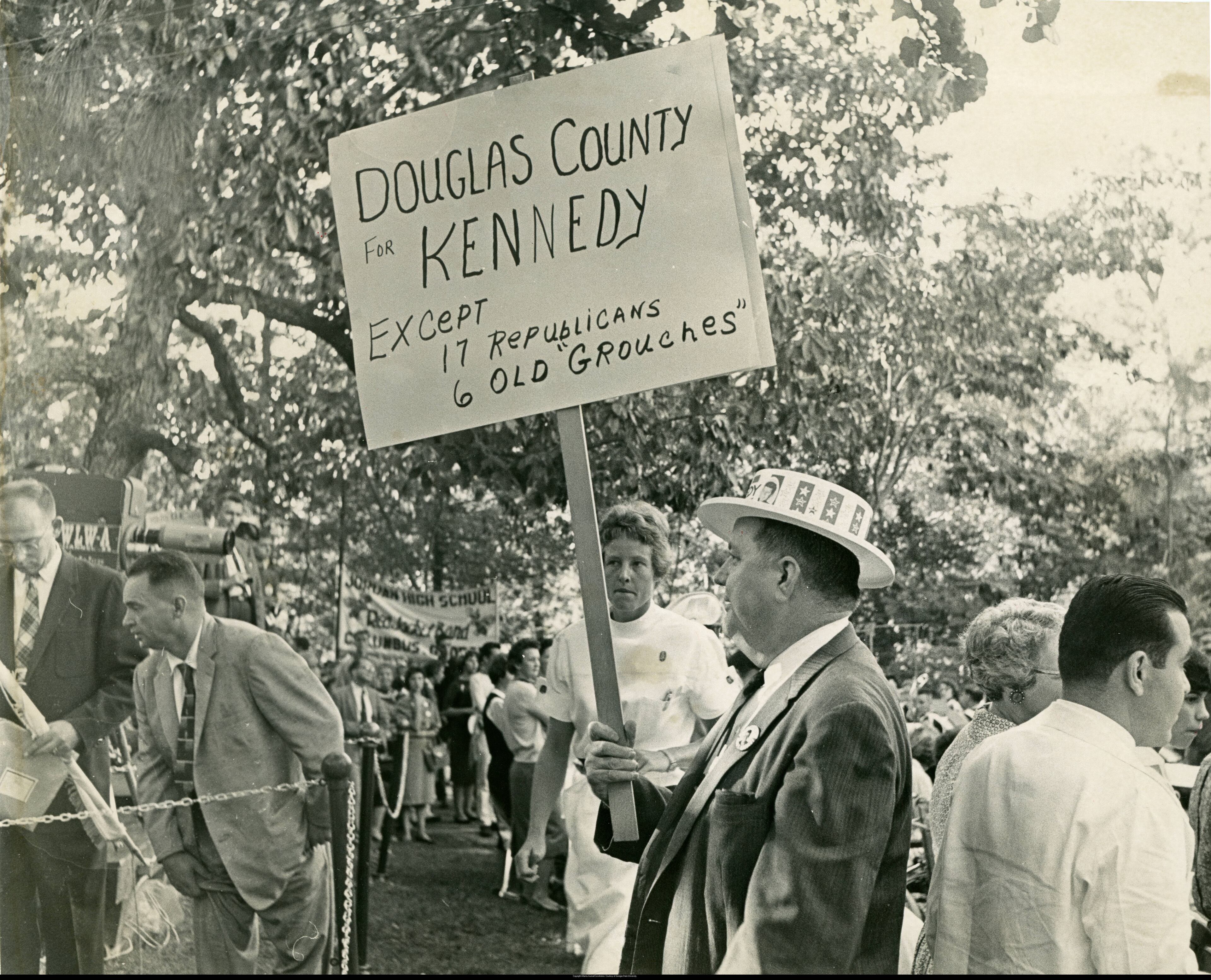 John F. Kennedy campaign supporter, carrying a sign that reads "Douglas County for Kennedy, except 17 Republicans, 6 old grouches'," Warm Springs, Georgia, October 10, 1960. Atlanta Journal-Constitution Photographic Archive