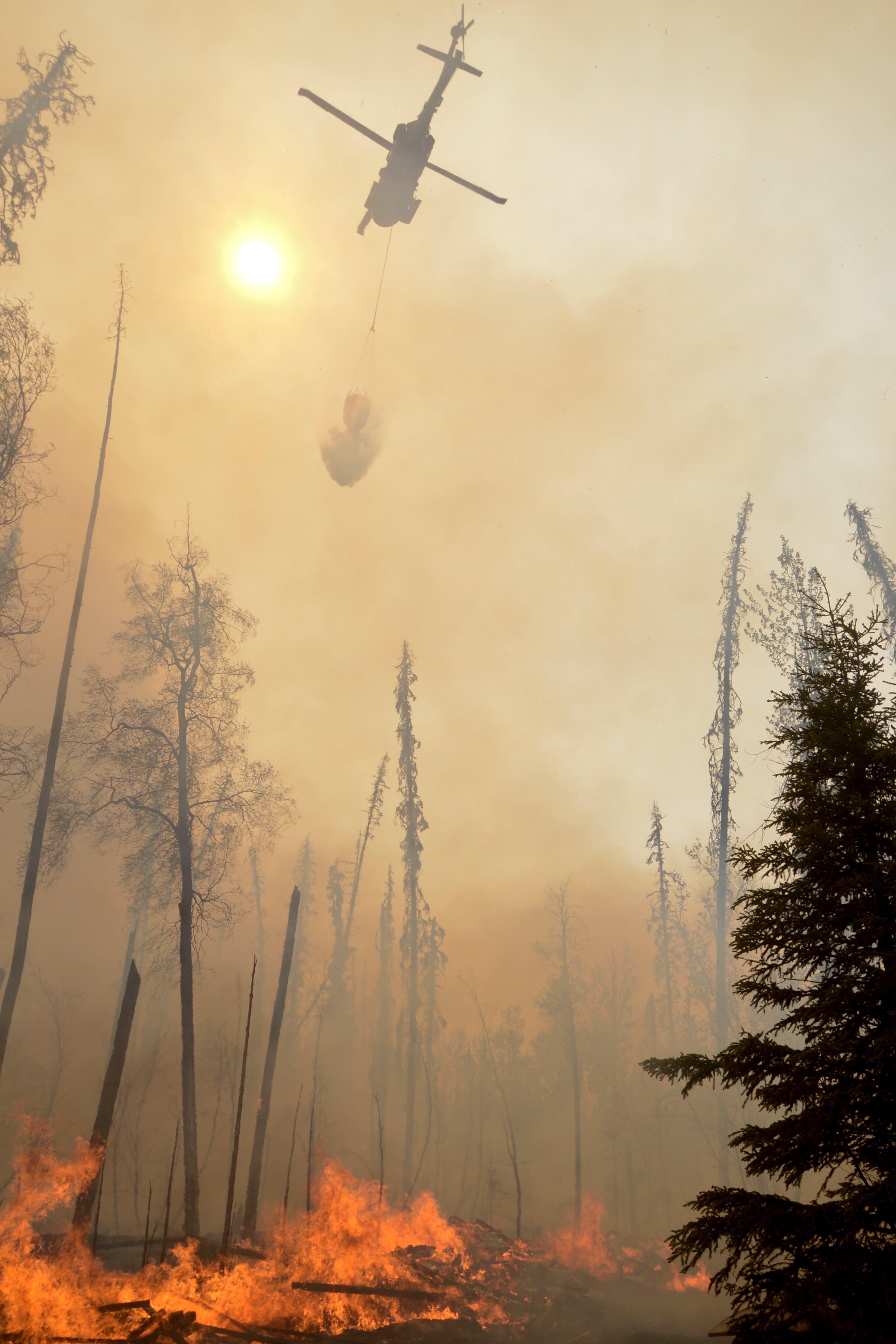 A helicopter dumps water on a portion of the Funny River Fire, Sunday, May 25, 2014, in the Funny River community in Soldotna, Alaska. The wildfire that has spread through the forest of Alaska's Kenai Peninsula has expanded in size, prompting authorities to order the evacuation of 1,000 structures, officials said. (AP Photo/Peninsula Clarion, Rashah McChesney)