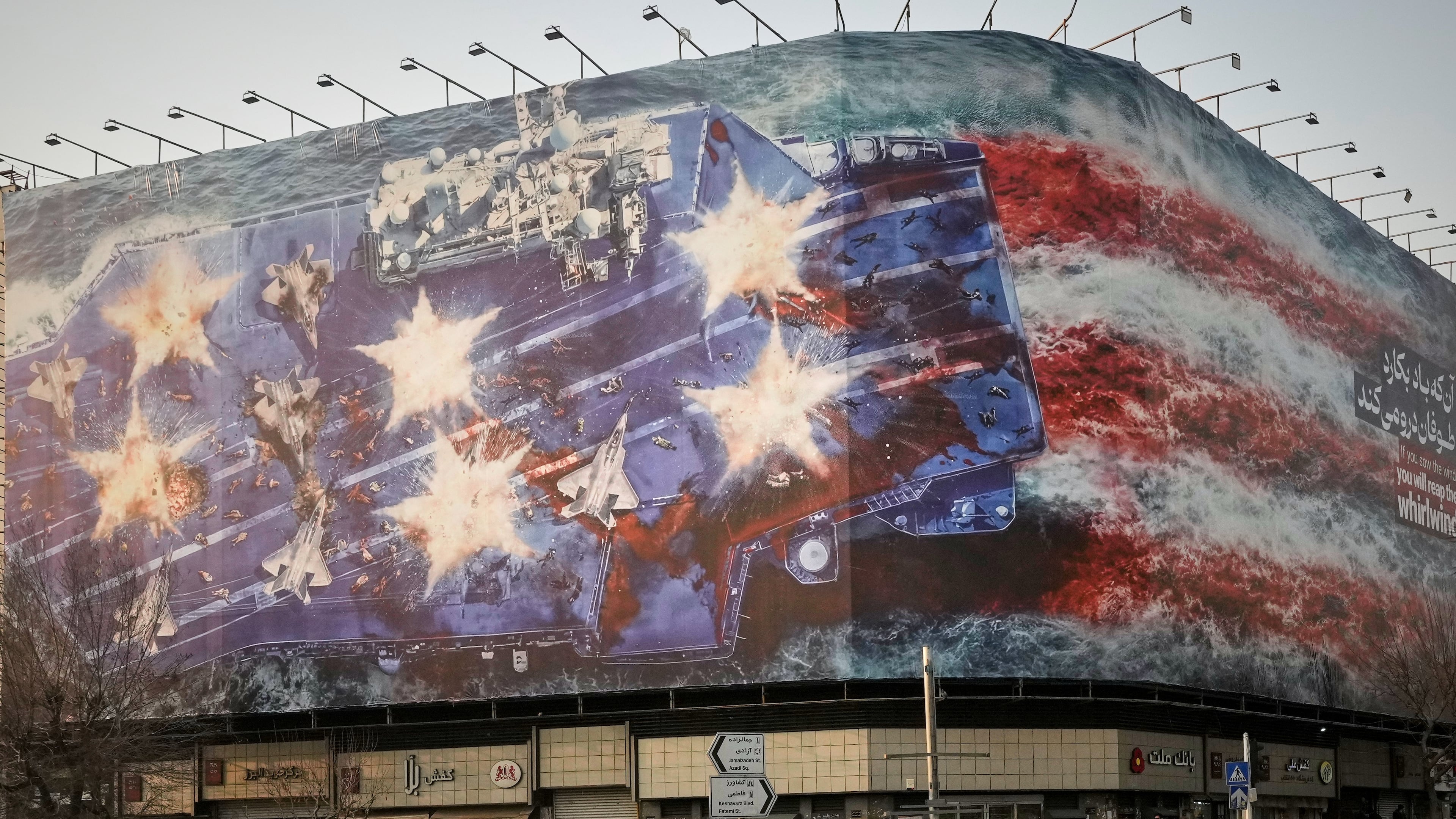 A billboard depicting a damaged U.S. aircraft carrier with disabled fighter jets on its deck and a sign reading in Farsi and English, "If you sow the wind, you'll reap the whirlwind," is seen at Enqelab-e-Eslami (Islamic Revolution) Square in Tehran, Iran, Sunday, Jan. 25, 2026. (AP Photo/Vahid Salemi)