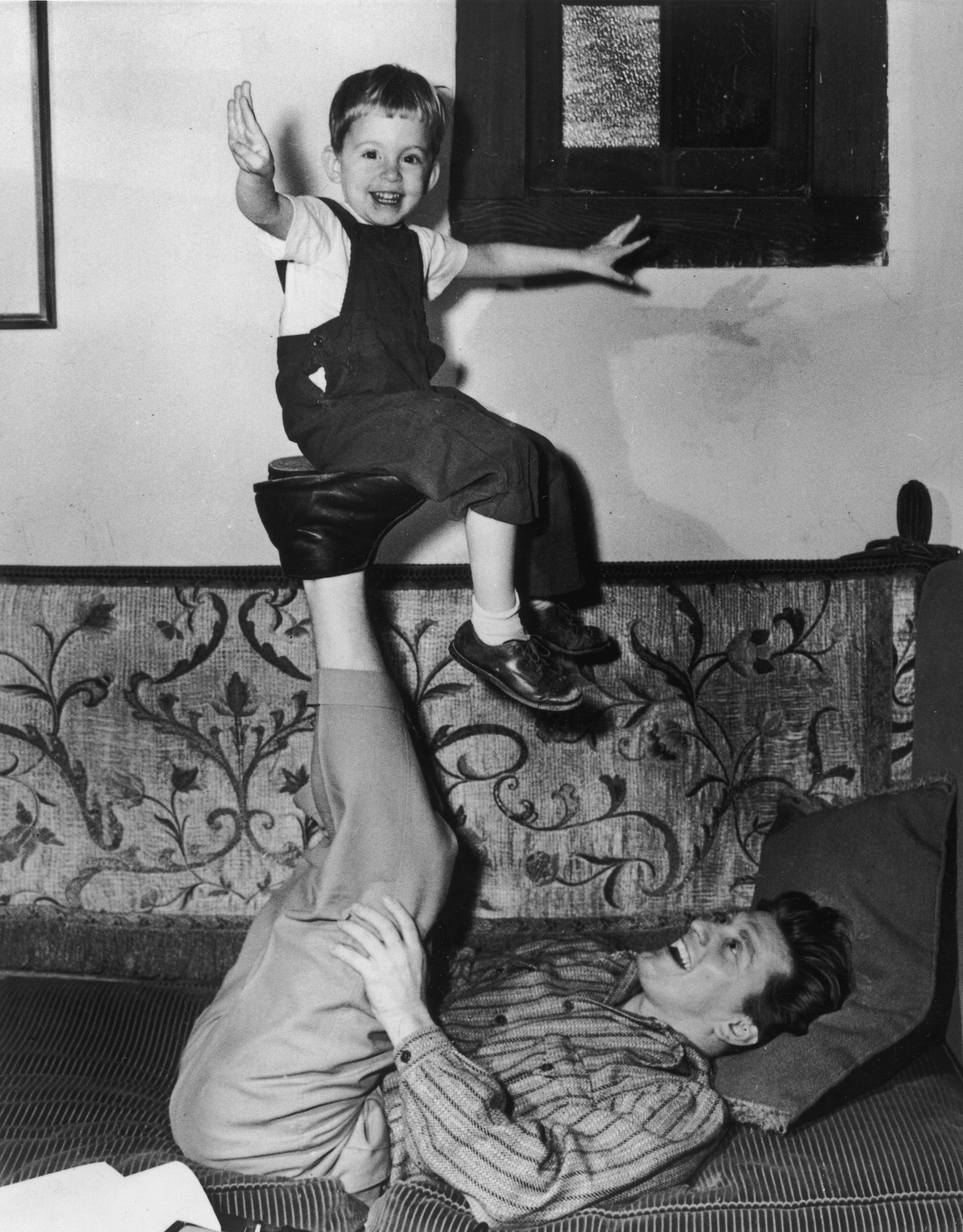 1948: American actor Kirk Douglas lying on a couch with his legs in the air as he balances his son, Michael on the soles of his feet. (Photo by Hulton Archive/Getty Images)