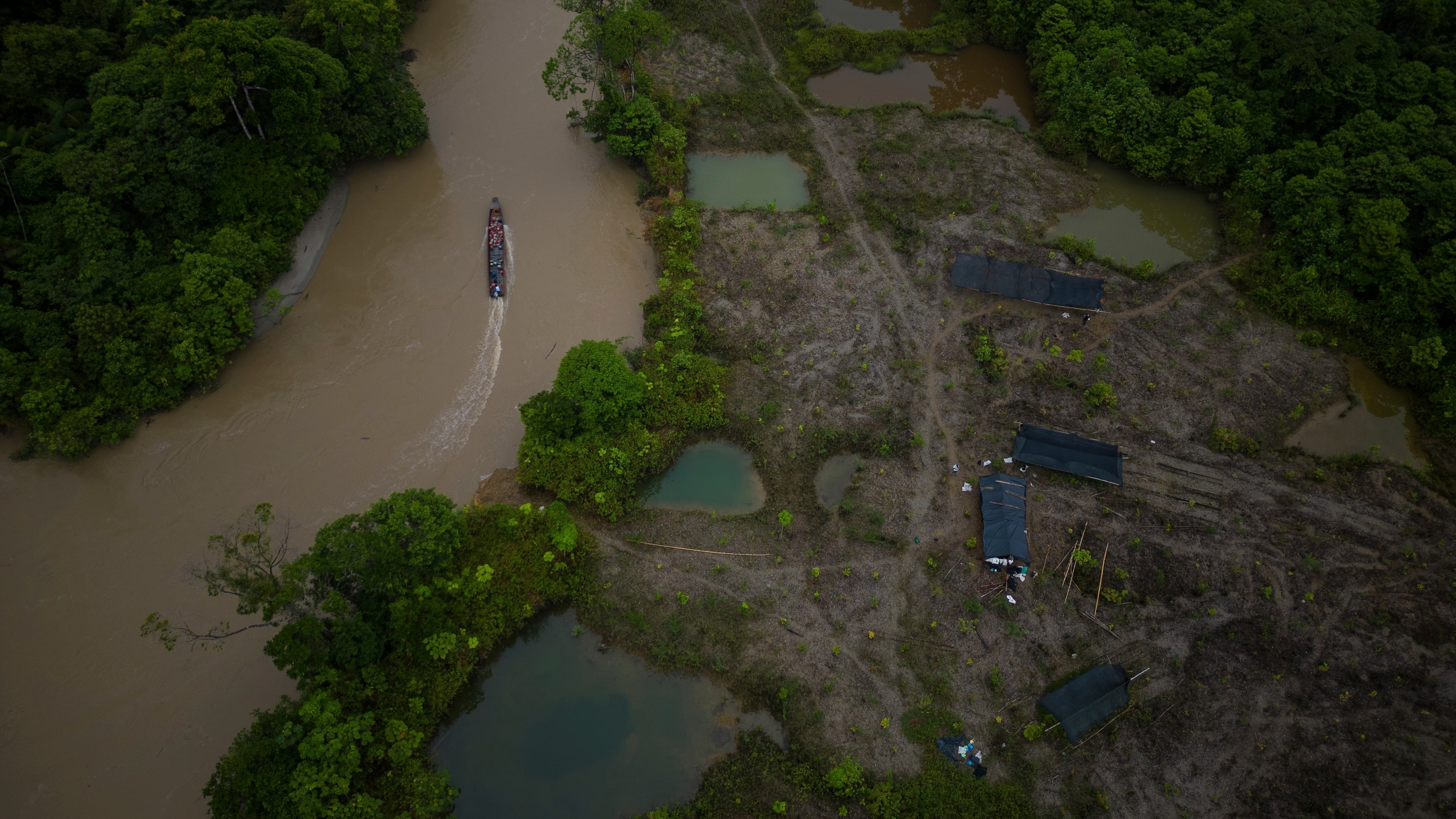 FILE - A boat, with gasoline to be taken to illegal mining machinery, maneuvers past an area that was mined and is being reforested by Asociacion Nuestra Casa Comun, or Our Community House Association, near Paimado, Colombia, Sept. 24, 2024. (AP Photo/Ivan Valencia, File)