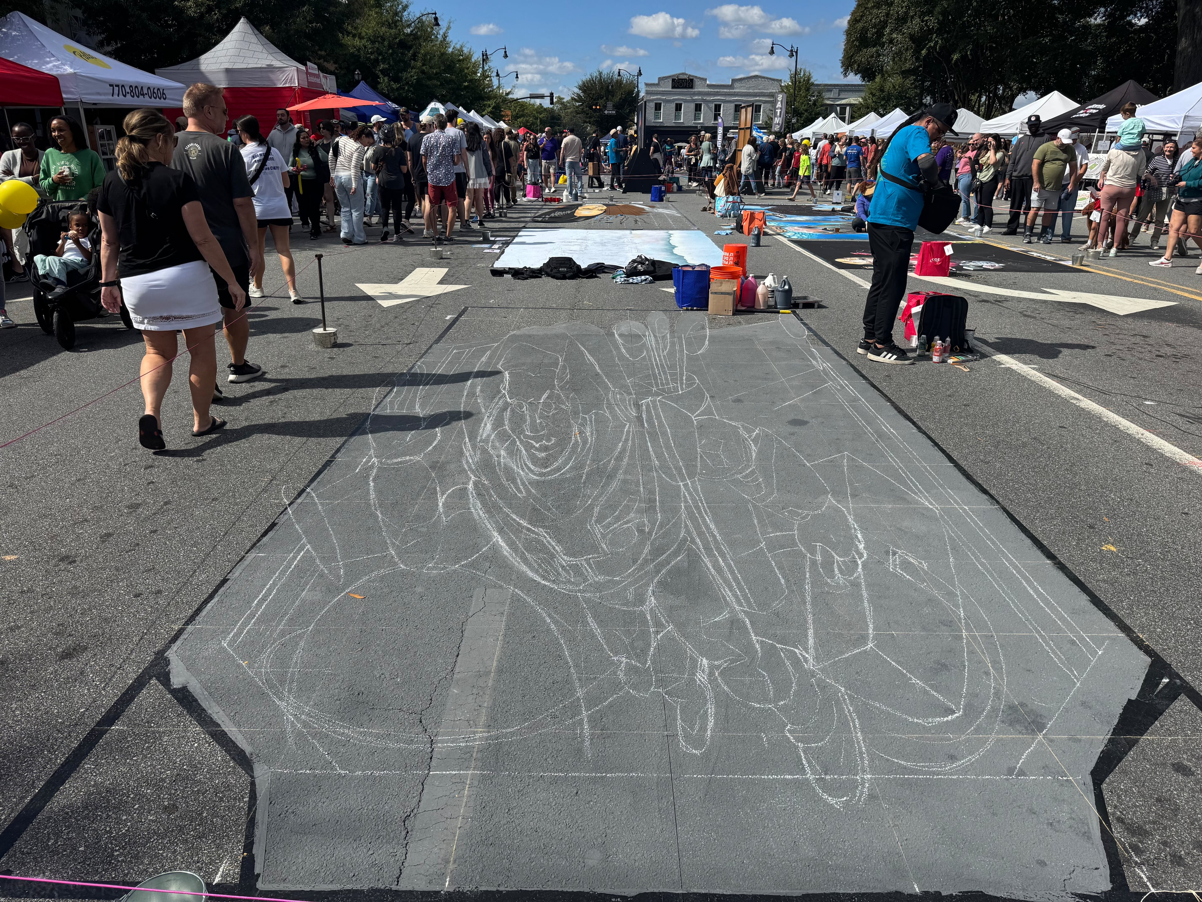 Artists from around the globe are doing work at Chalktoberfest in Marietta. Pictured is an outline of chalk art being worked on Saturday, Oct. 11, 2025, by Ruven Poncia, who is based in Utrecht, Netherlands. (Caleb Groves/AJC)