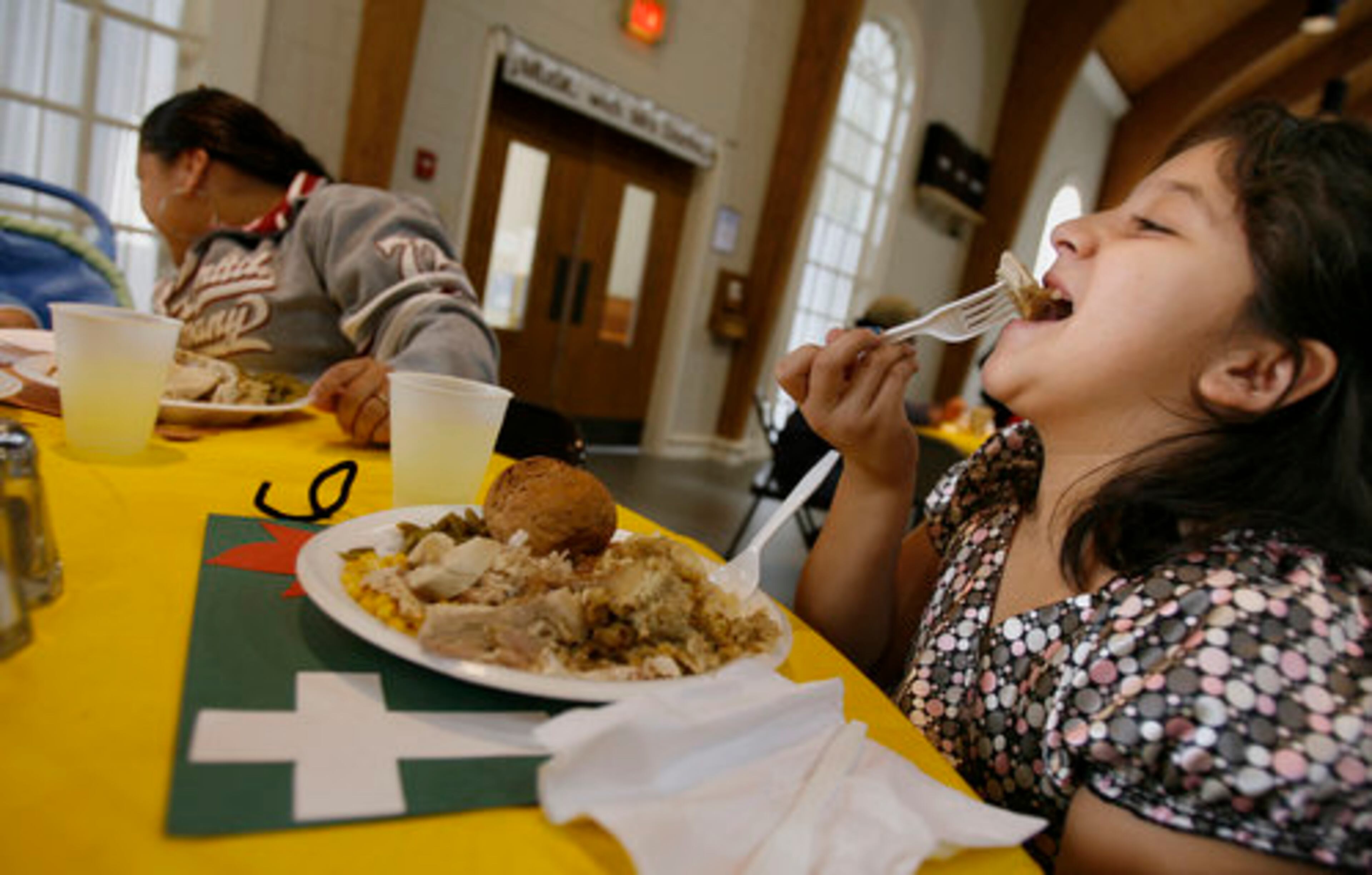 Celia Luhan, 9, of Cumming enjoys her turkey at the annual Thanksgiving dinner at Cumming First United Methodist Church while her cousin Carolina Luhan looks after a baby. This is the eighth year the church has served food to community members on Thanksgiving.