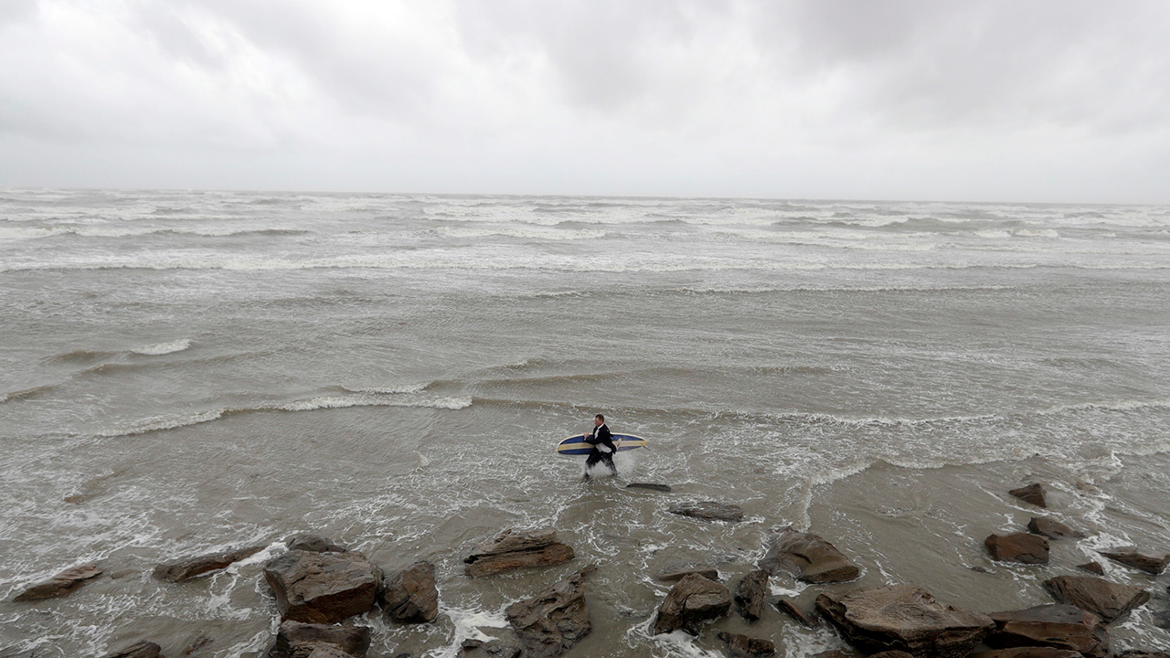 Mark Metzger carries his surfboard through the water in Galveston, Texas as Hurricane Harvey intensifies in the Gulf of Mexico Friday, Aug. 25, 2017. Harvey is forecast to be a major hurricane when it makes landfall along the middle Texas coastline. (AP Photo/David J. Phillip)