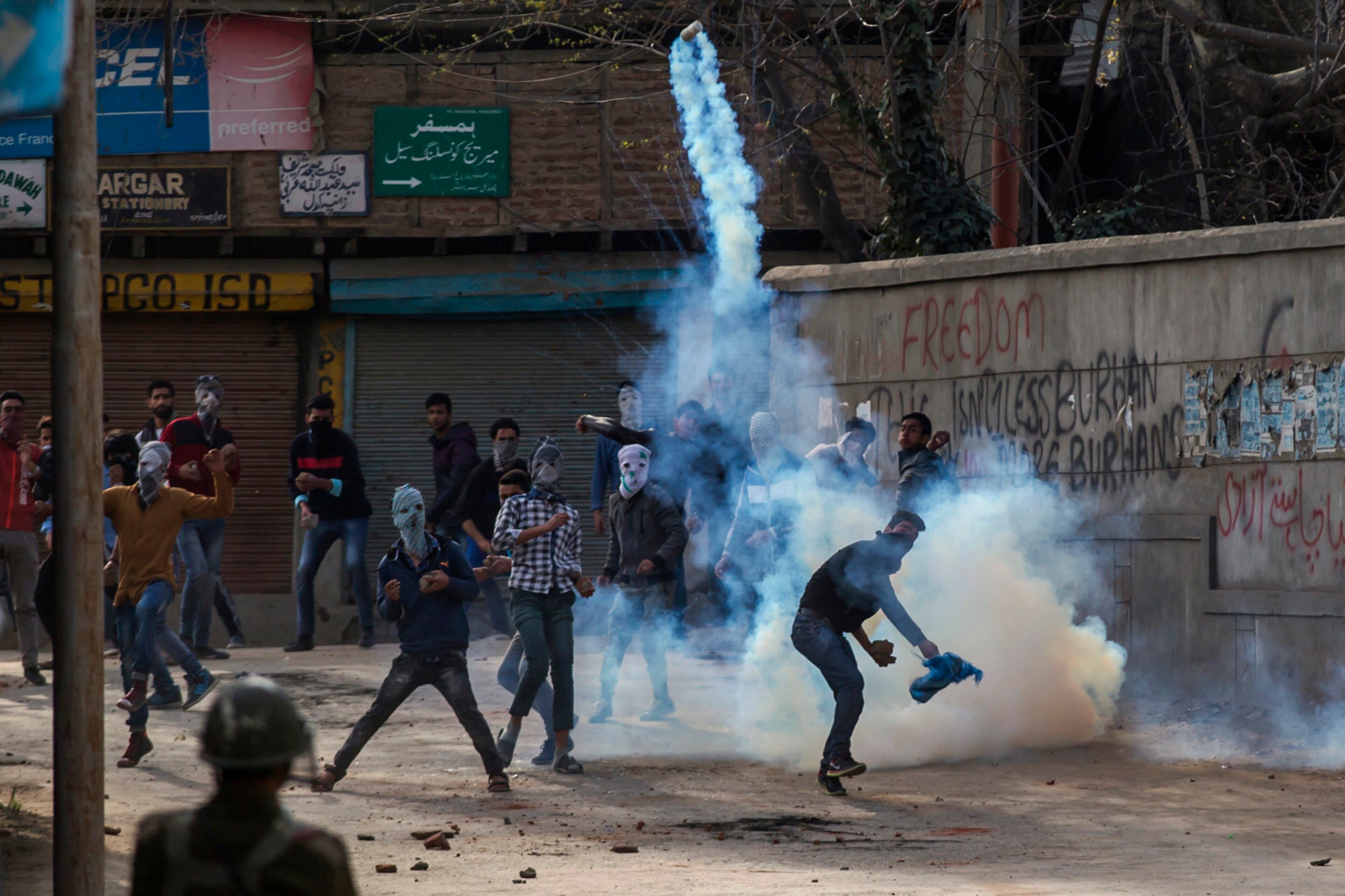 A masked protester throws an exploded tear gas shell back at Indian policemen in Srinagar, Indian controlled Kashmir, Wednesday, March 29, 2017. Shops and business establishment remained closed Wednesday in Indian-controlled Kashmir after separatists called for a strike against the killing of three civilians during anti-India protests near the site of a gunbattle on Tuesday. (AP Photo/Dar Yasin)