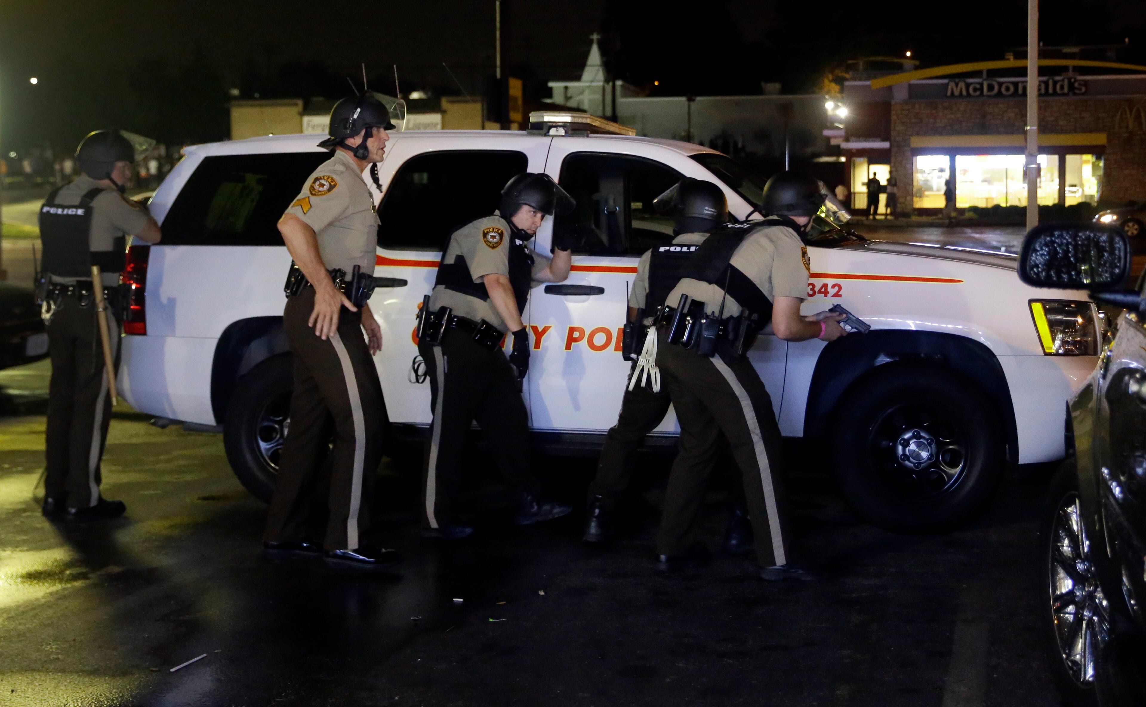 Members of the St. Louis County Police Department take cover at a protest in Ferguson, Mo., Sunday, Aug. 9, 2015. The one-year anniversary of Michael Brown's death in Ferguson began with a march in his honor and ended with a protest that was interrupted by gunfire. (AP Photo/Jeff Roberson)