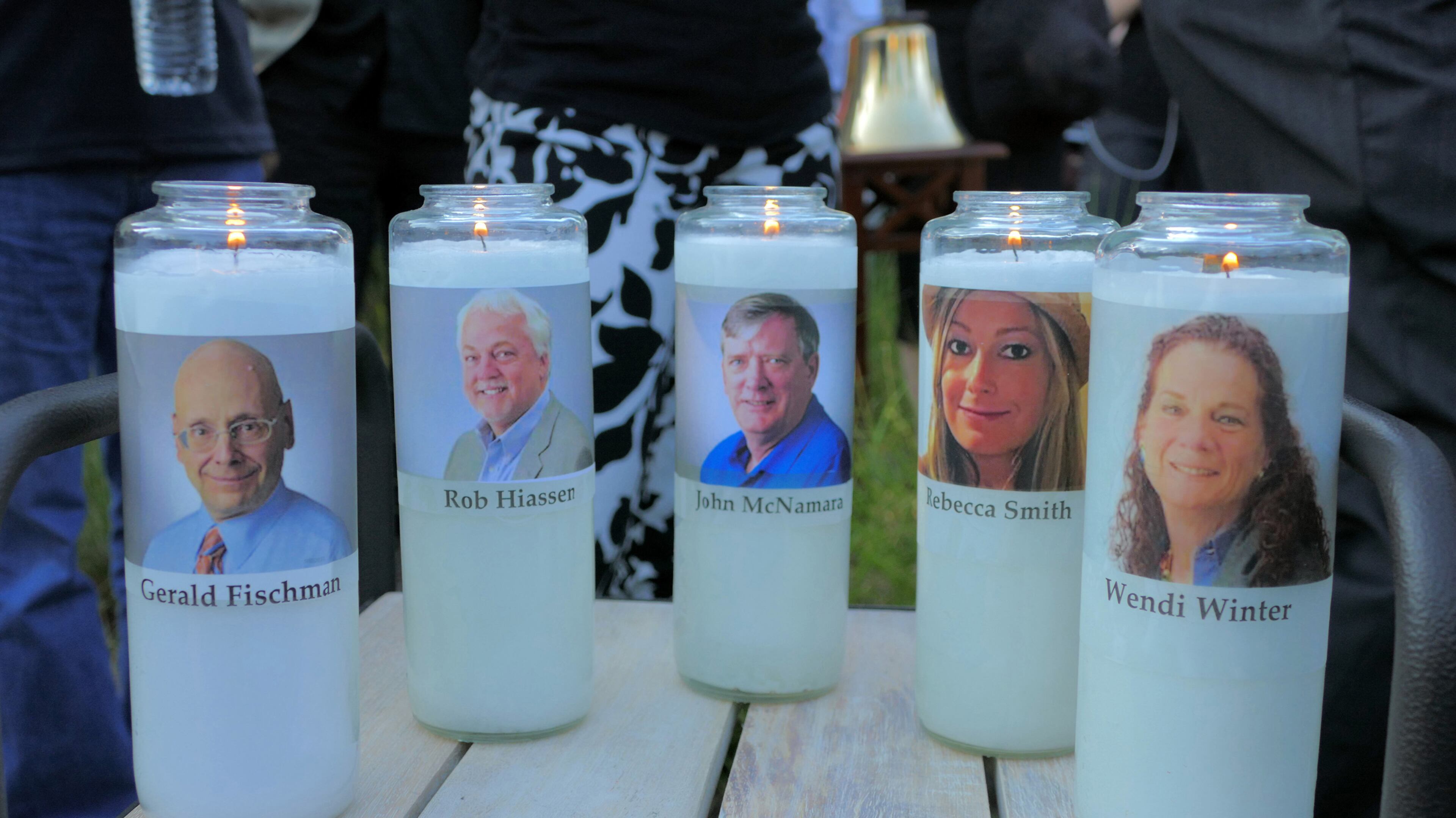 In this file photo from June 29, 2018, candles honoring Gerald Fischman, Rob Hiassen, John McNamara, Rebecca Smith, and Wendi Winters flicker as the sun sets during a candlelight vigil at Annapolis Mall for the five Capital Gazette employees slain during a shooting spree in their newsroom.