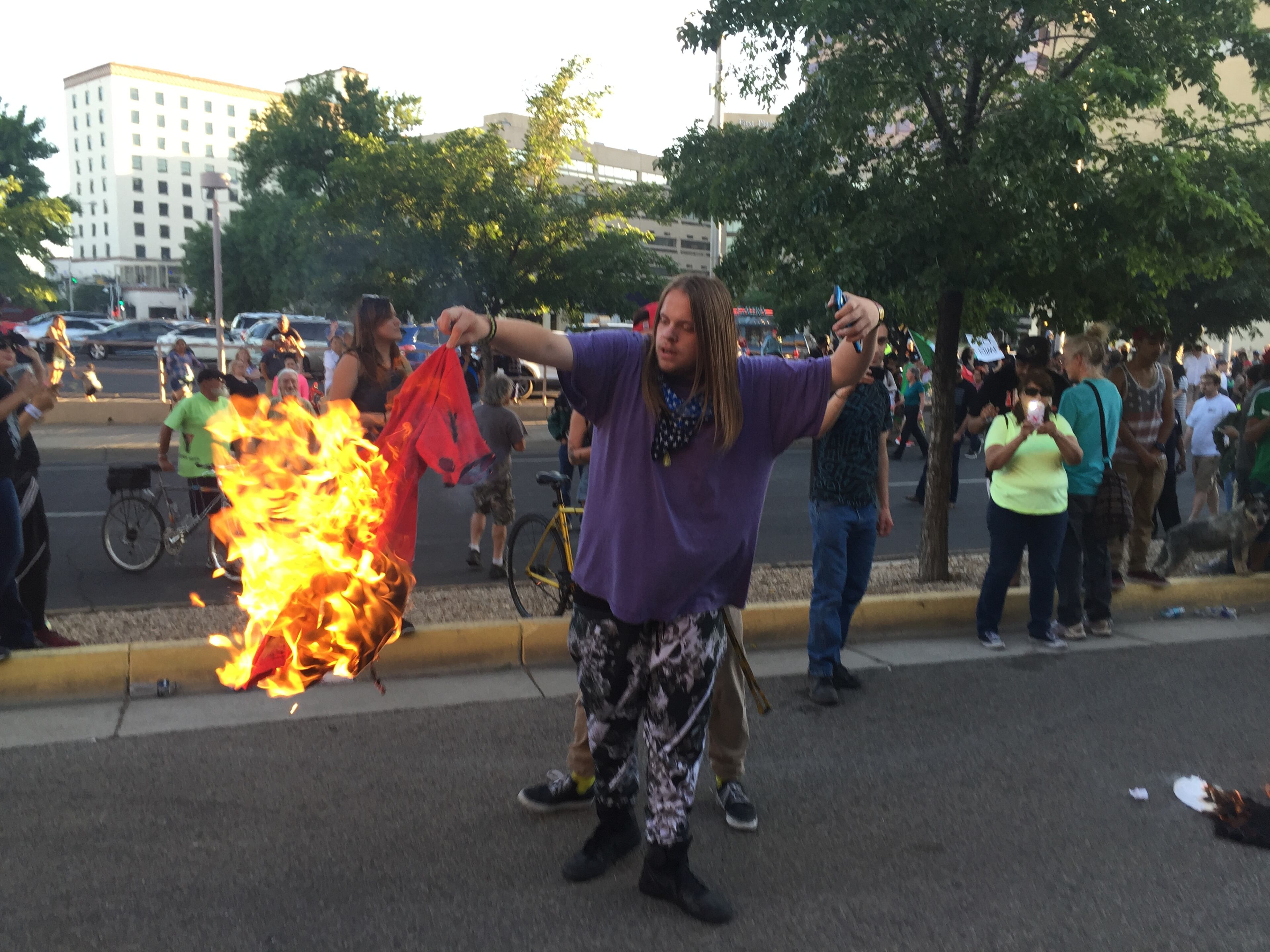 A protestor of Republican presidential candidate Donald Trump holds a burning T-shirt as hundreds of people protest outside a rally for Trump in Albuquerque, Tuesday, May 24, 2016. (AP Photo/Russell Contreras)