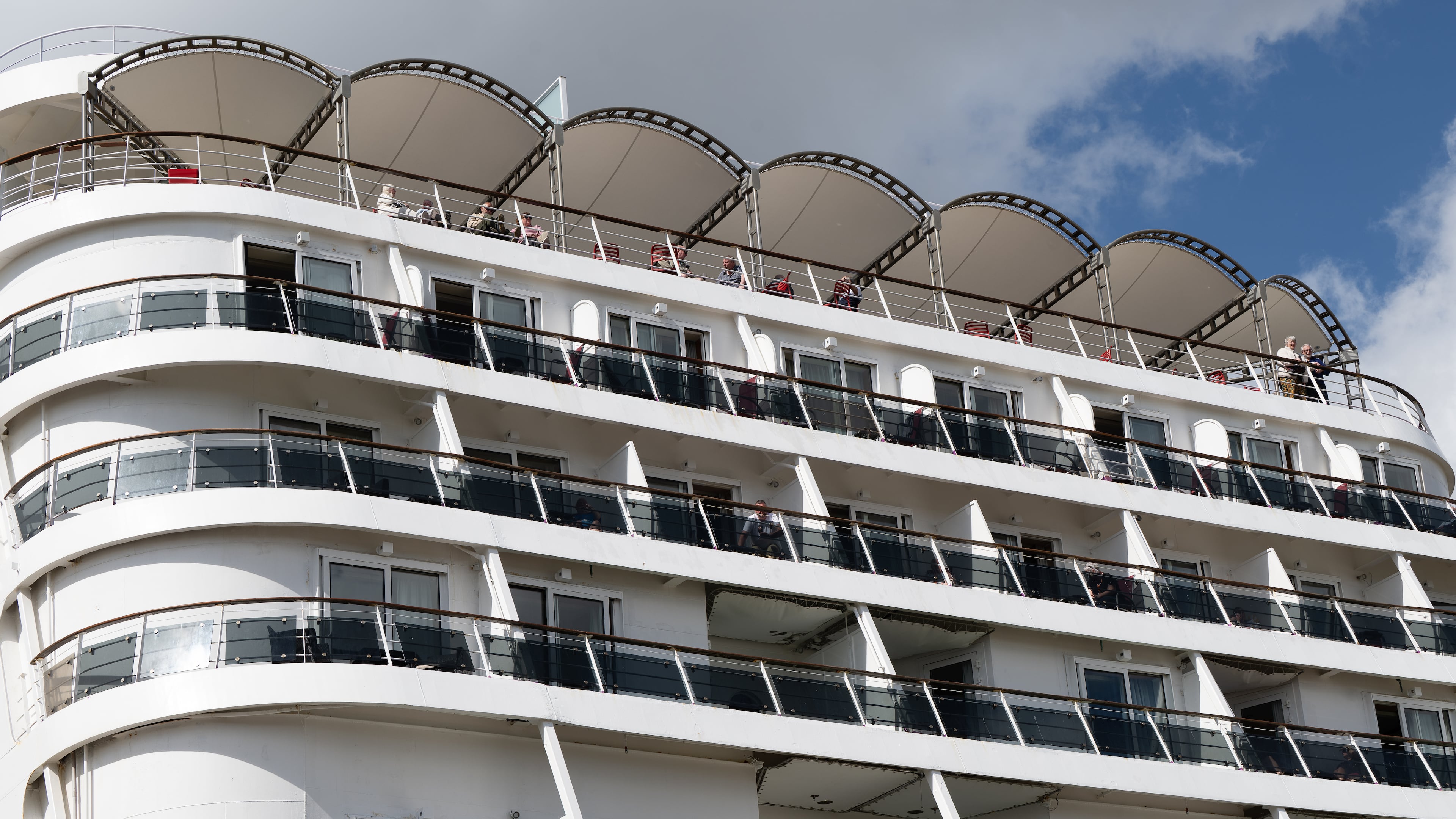 Passengers stand aboard the British cruise ship Ambition, as French authorities have ordered 1,700 passengers and crew to stay on board due to a gastrointestinal illness outbreak, in Bordeaux, southwestern France, Wednesday, May 13, 2026. (AP Photo/Caroline Blumberg)