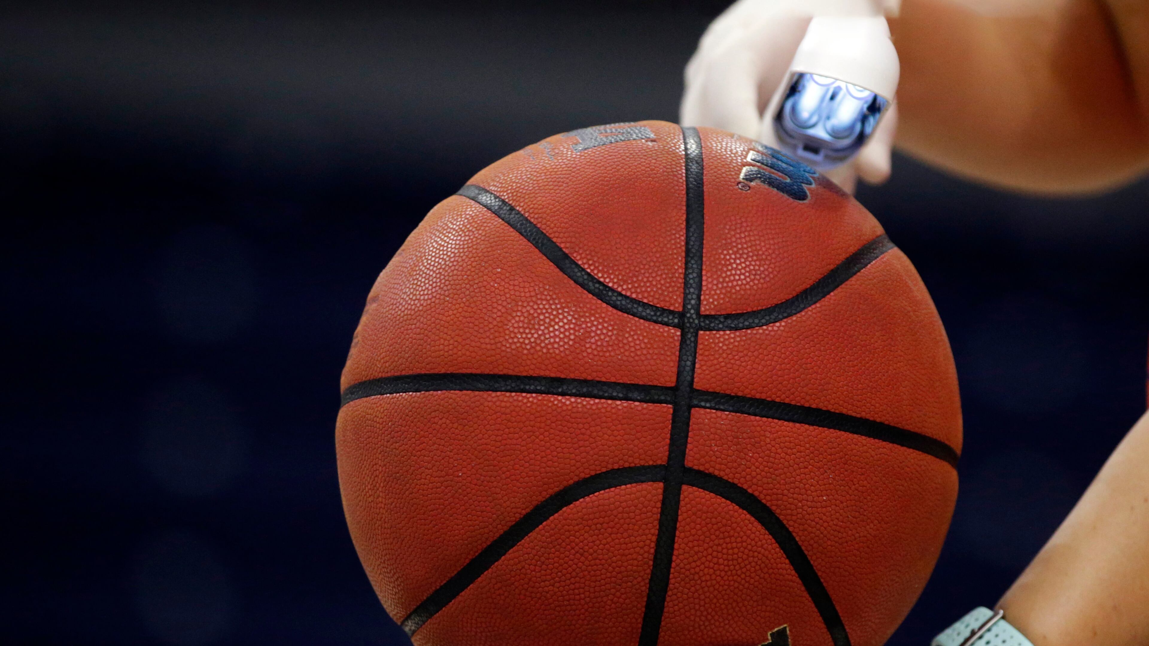 An worker waves an ultra violet lamp over the ball to kill germs during an NCAA basketball game. (Butch Dill/AP)