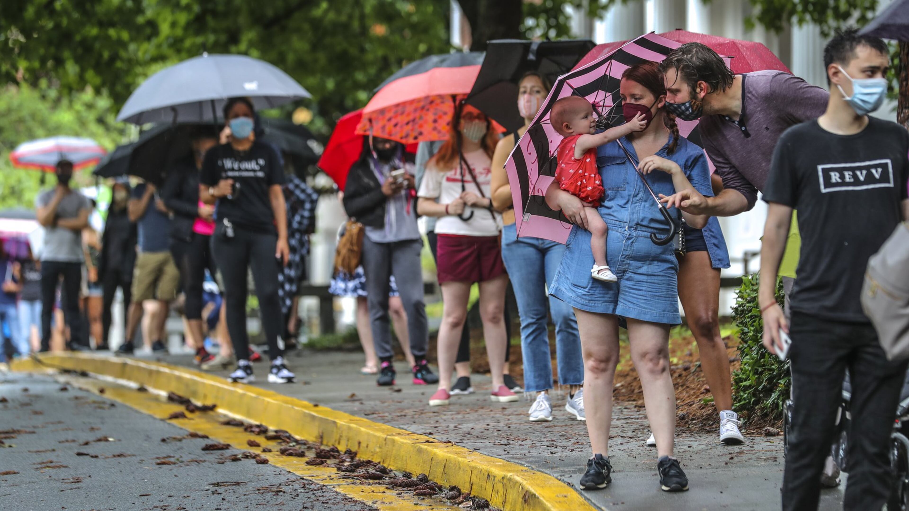 Amanda McElveen holds 1-year old Luna, left, as Justin McElveen interacts while they and other voters stand in line in the rain at Garden Hills Elementary School in Atlanta on Friday, the last day of early voting for the Georgia primary. Lines lasted for hours in some places. JOHN SPINK/JSPINK@AJC.COM