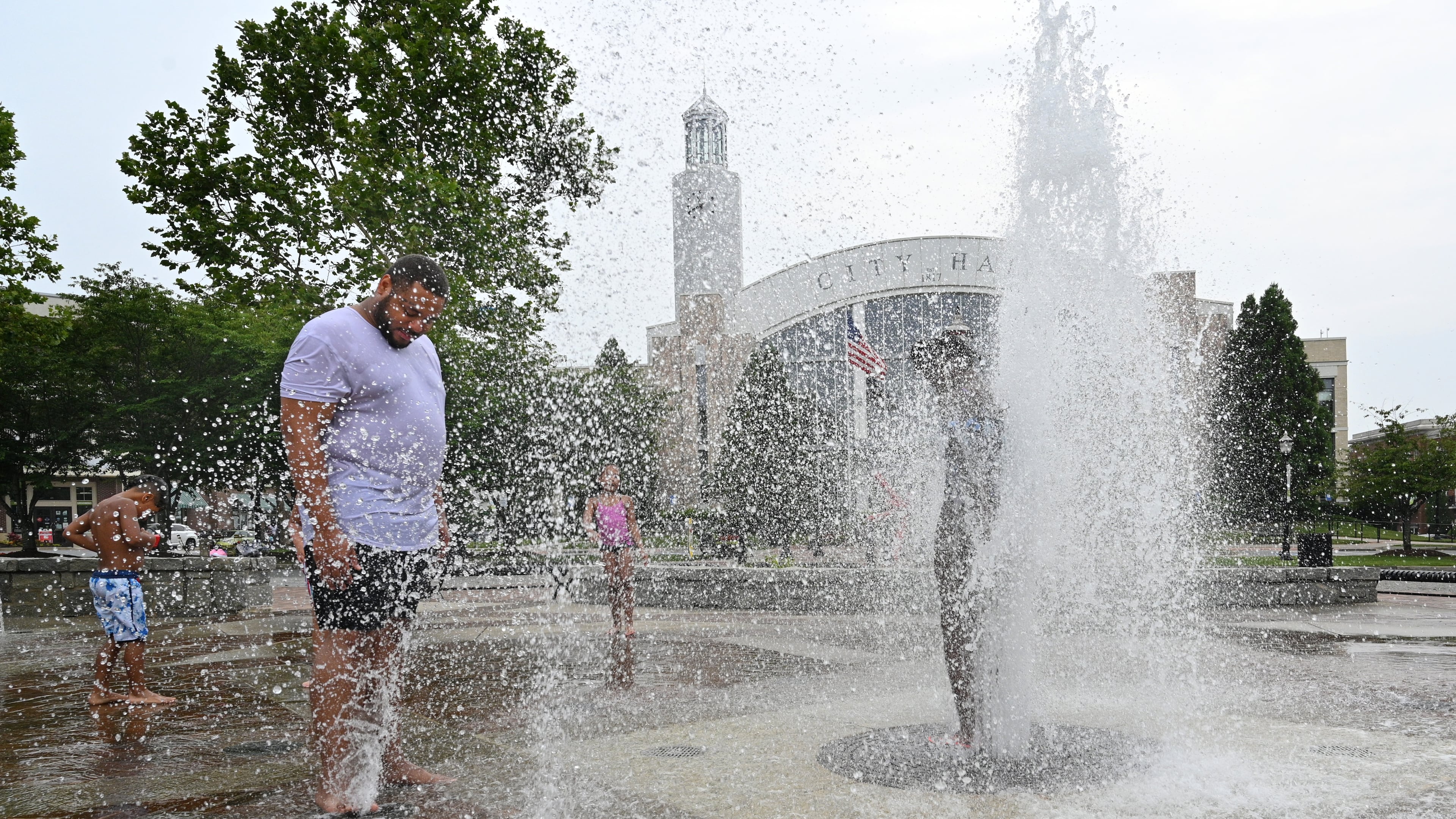 Adam Parker (left), of Suwanee, and his children play in the splash fountain at Town Center Park, Friday, June 30, 2023, in Suwanee. (Hyosub Shin/AJC)