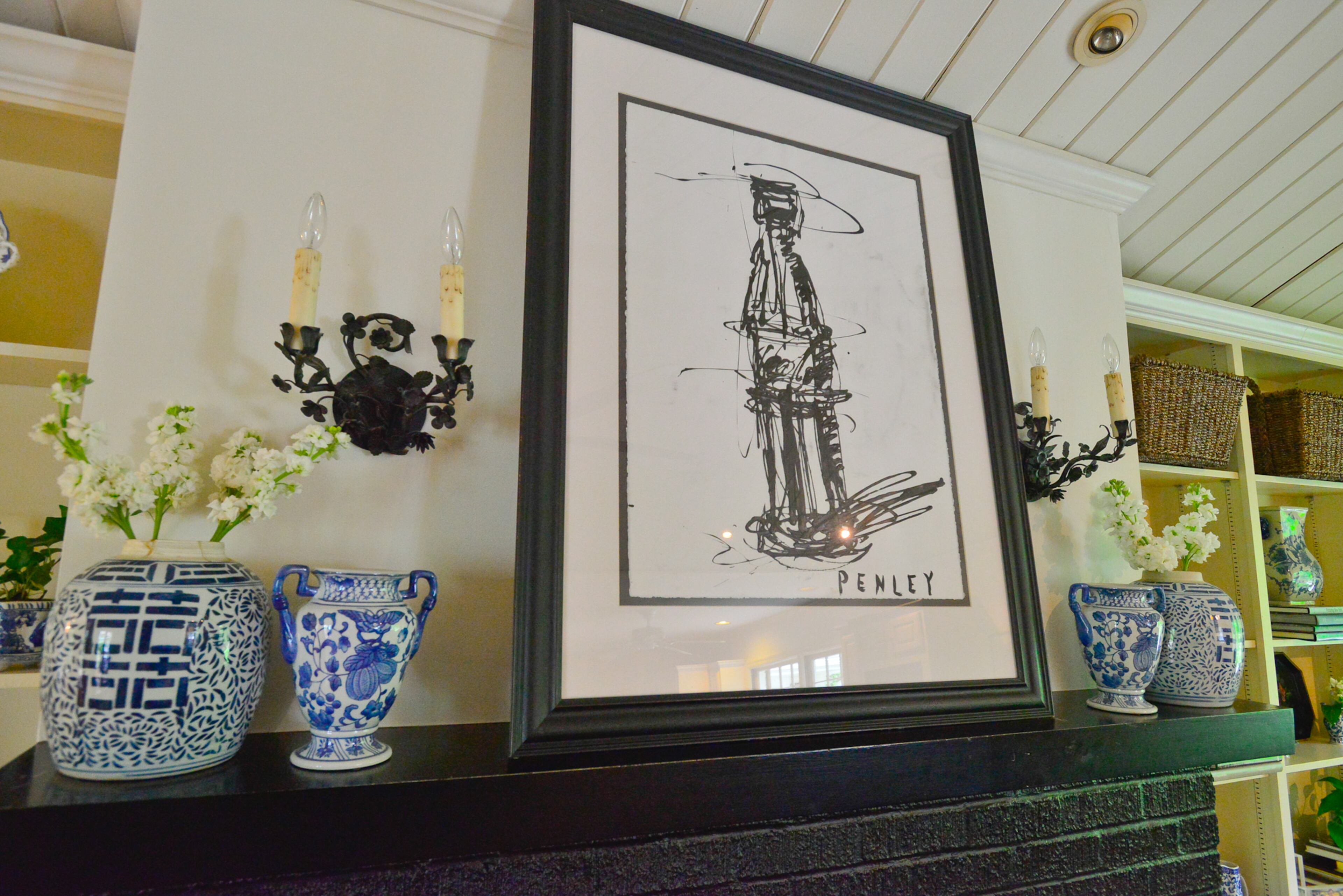 A Steve Penley painting of a Coke bottle and blue-and-white china fill the mantle of the fireplace in the family room, which has a vaulted ceiling with recessed lights.