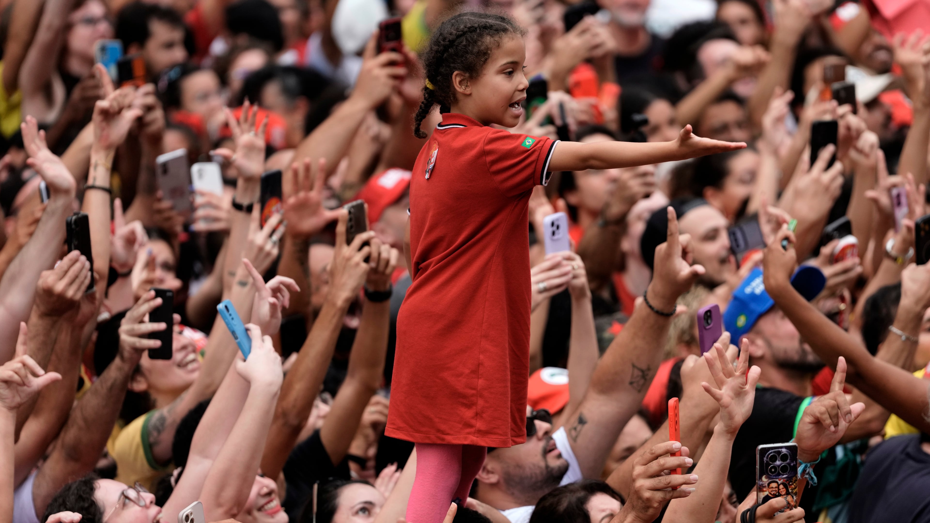 A girl standing on a man's shoulders reaches out amid a crowd of supporters of Brazilian President Luiz Inacio Lula da Silva, who is running for reelection, during his final campaign rally, a day ahead of the presidential runoff election in Sao Paulo, Brazil, Saturday, Oct. 24, 2026. (AP Photo/Natacha Pisarenko)