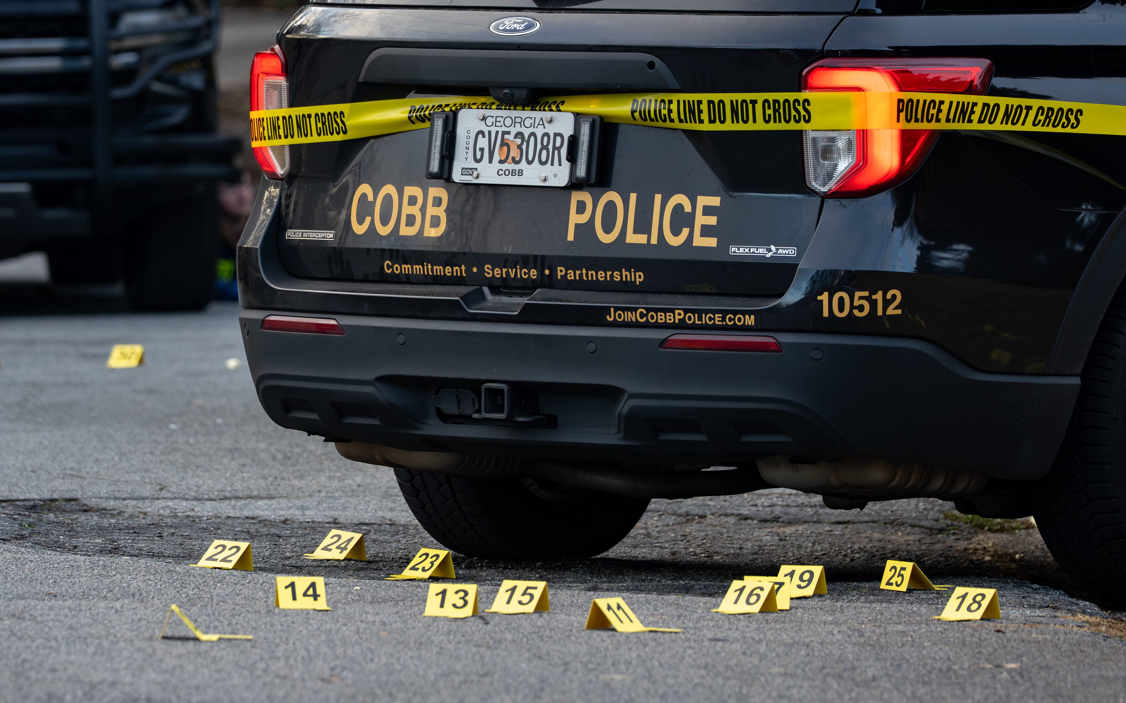 Crime scene markers sit behind a police vehicle after Cobb County officers shot a man. (Ben Hendren for the AJC)
