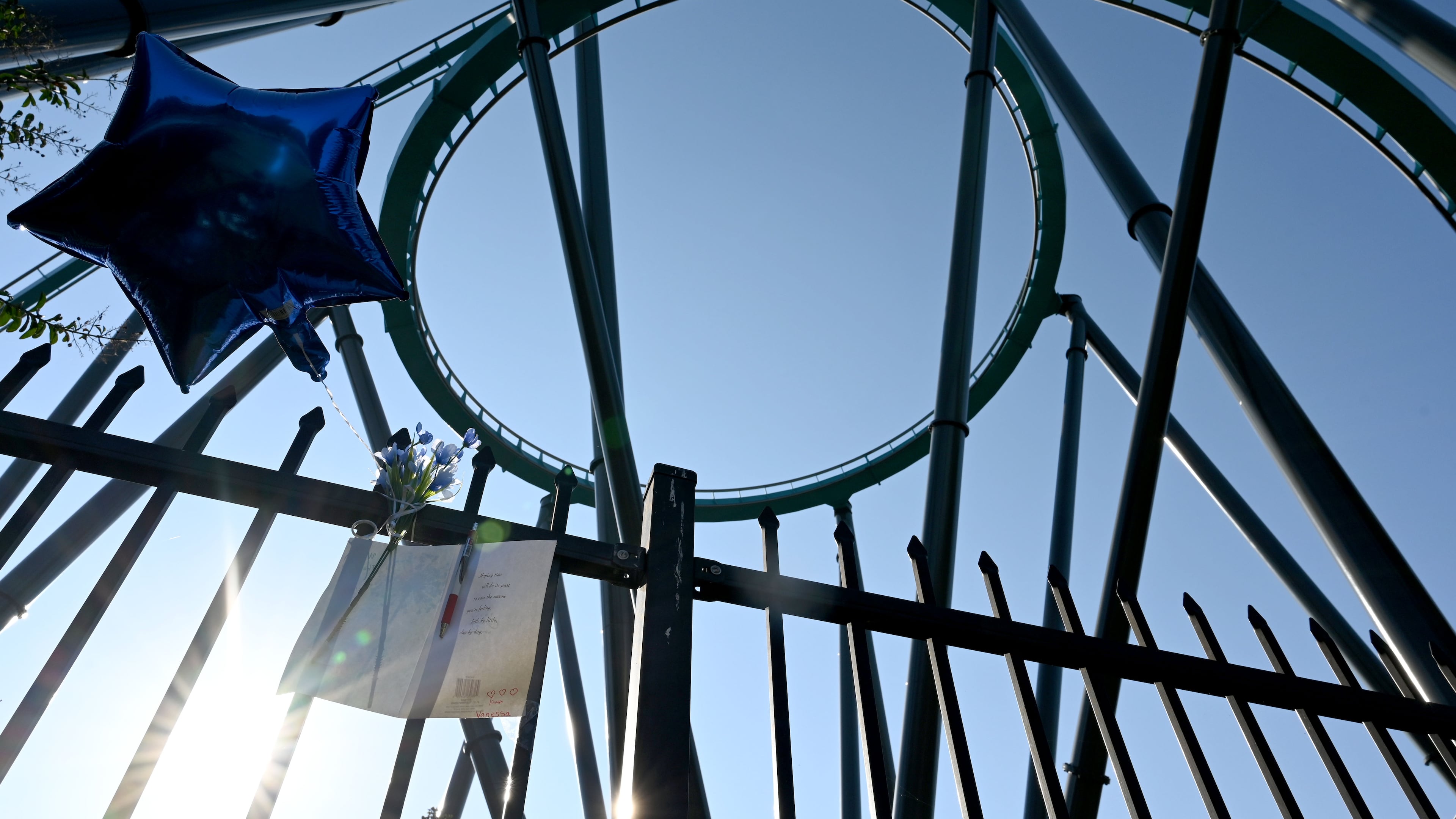 A memorial is displayed on the fence at Six Flags Over Georgia as the Goliath roller coaster is shown in the background on Thursday, Oct. 15, 2026. A 42-year-old Atlanta educator, Hassan Kariem, died after being ejected from the ride Oct. 12. (Hyosub Shin/AJC)
