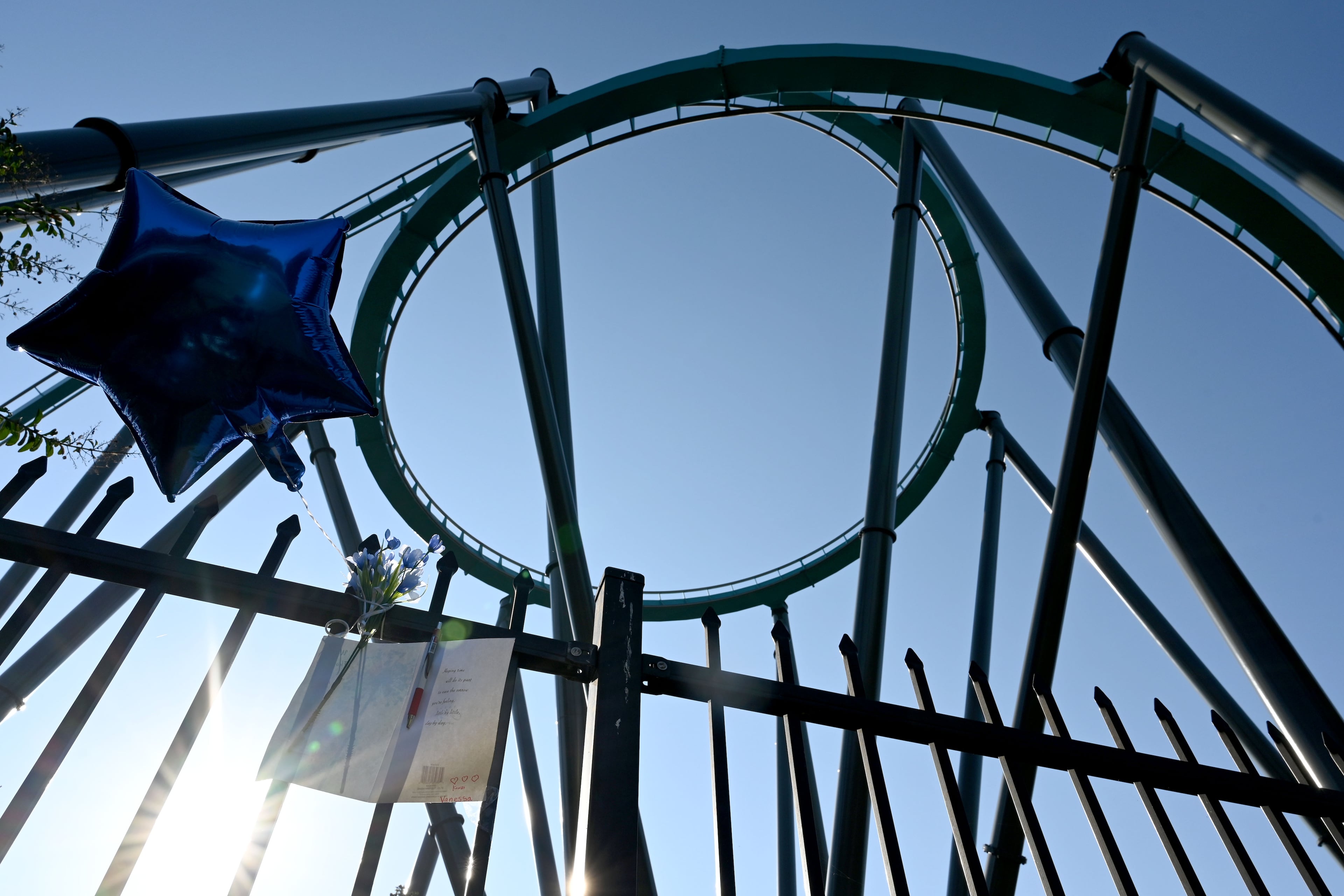 A memorial is displayed on the fence at Six Flags Over Georgia as the Goliath roller coaster is shown in the background on Thursday, Oct. 15, 2026. A 42-year-old Atlanta educator, Hassan Kariem, died after being ejected from the ride Oct. 12. (Hyosub Shin/AJC)