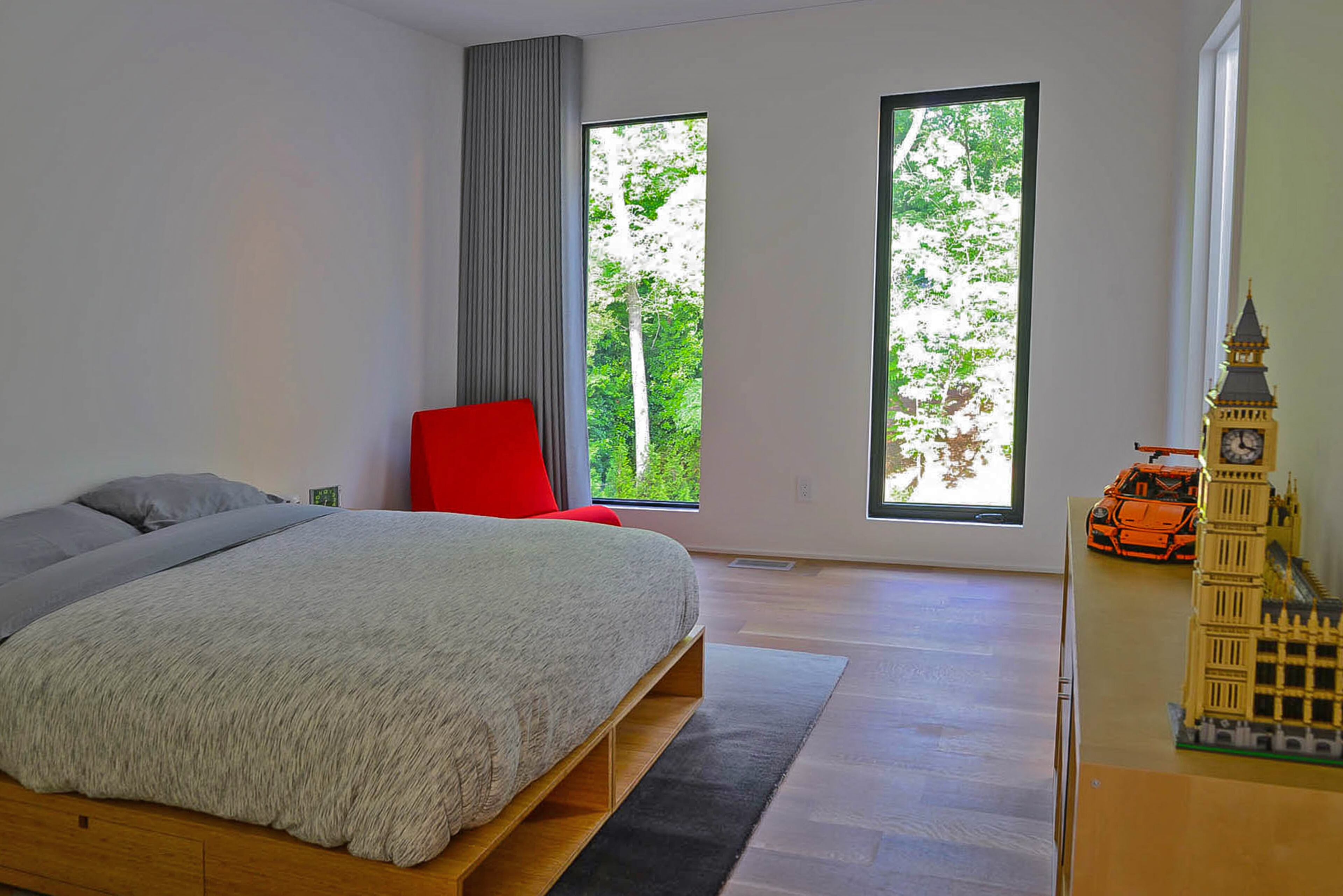 A bamboo Buden bed by Stem with gray bedding is joined by a red chair from Vitra in one of the children's bedrooms. The dresser displays Lego sets, including Big Ben and a Lego Technic Porsche.