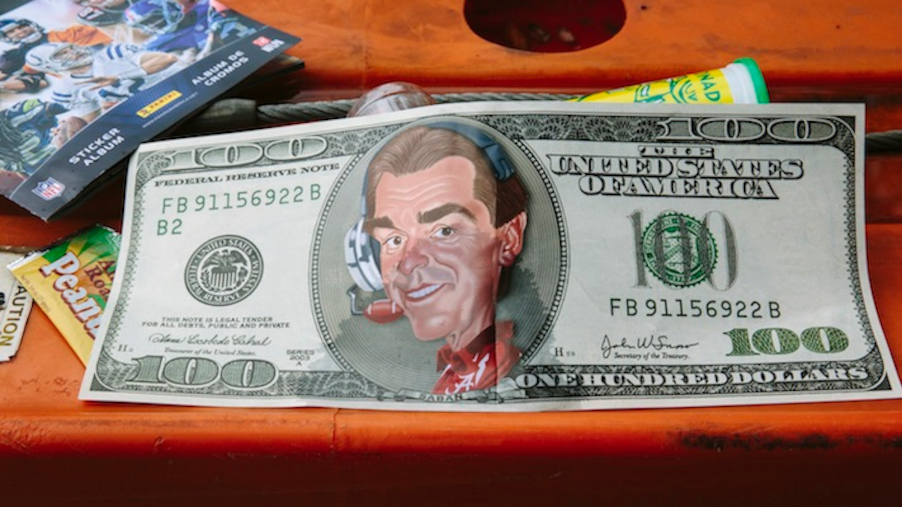 A poster of a mock $100 bill featuring a caricature of University of Alabama head football coach Nick Saban outside Bryant-Denny Stadium during homecoming weekend, in Tuscaloosa, Ala., Oct. 10, 2015. Over the past decade, the success of Alabama’s football program has become a powerful engine for the university’s economic and academic growth. (Edmund D. Fountain/The New York Times)