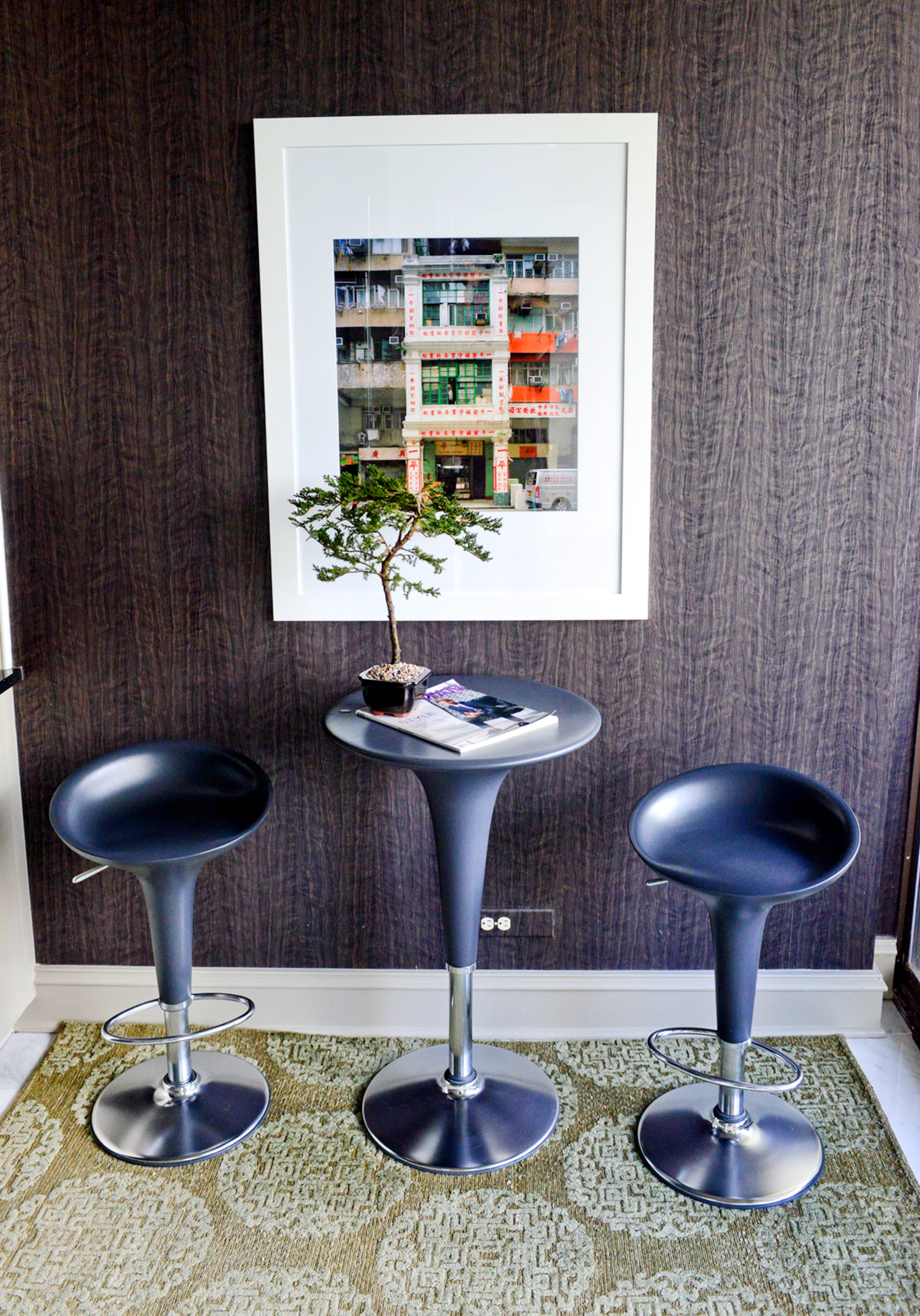 A dark blue table and chairs sit at the end of Jason Moattar's galley-style kitchen, offset by a rug from Moattar Ltd.. Above the table hangs a photograph featured in the book "Tilting the Lens: Telling the Story of Sham Shui Po," which features the work of SCAD students and professors.