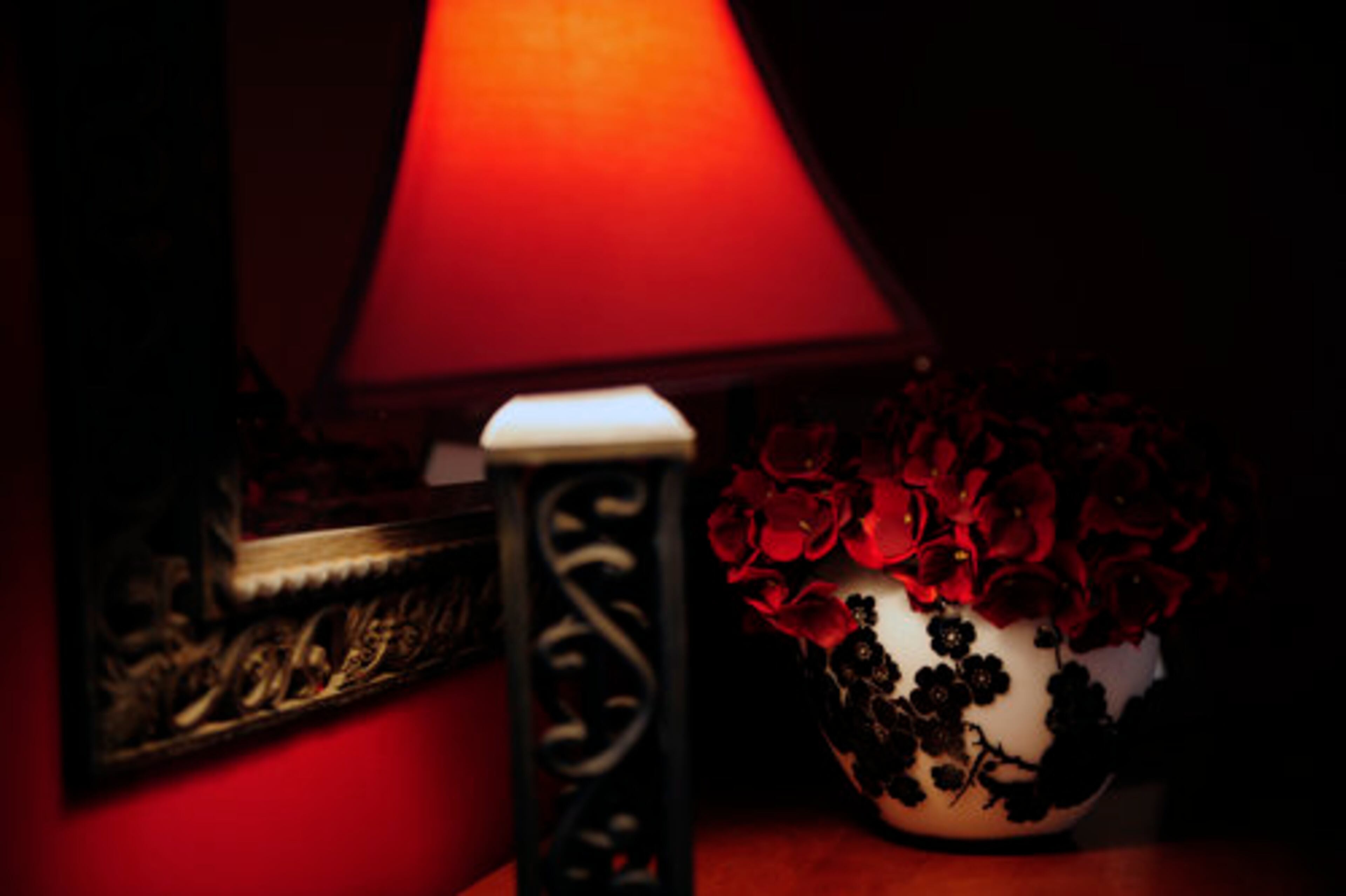 A lamp with a red shade glows next to a vase of roses in her bedroom.