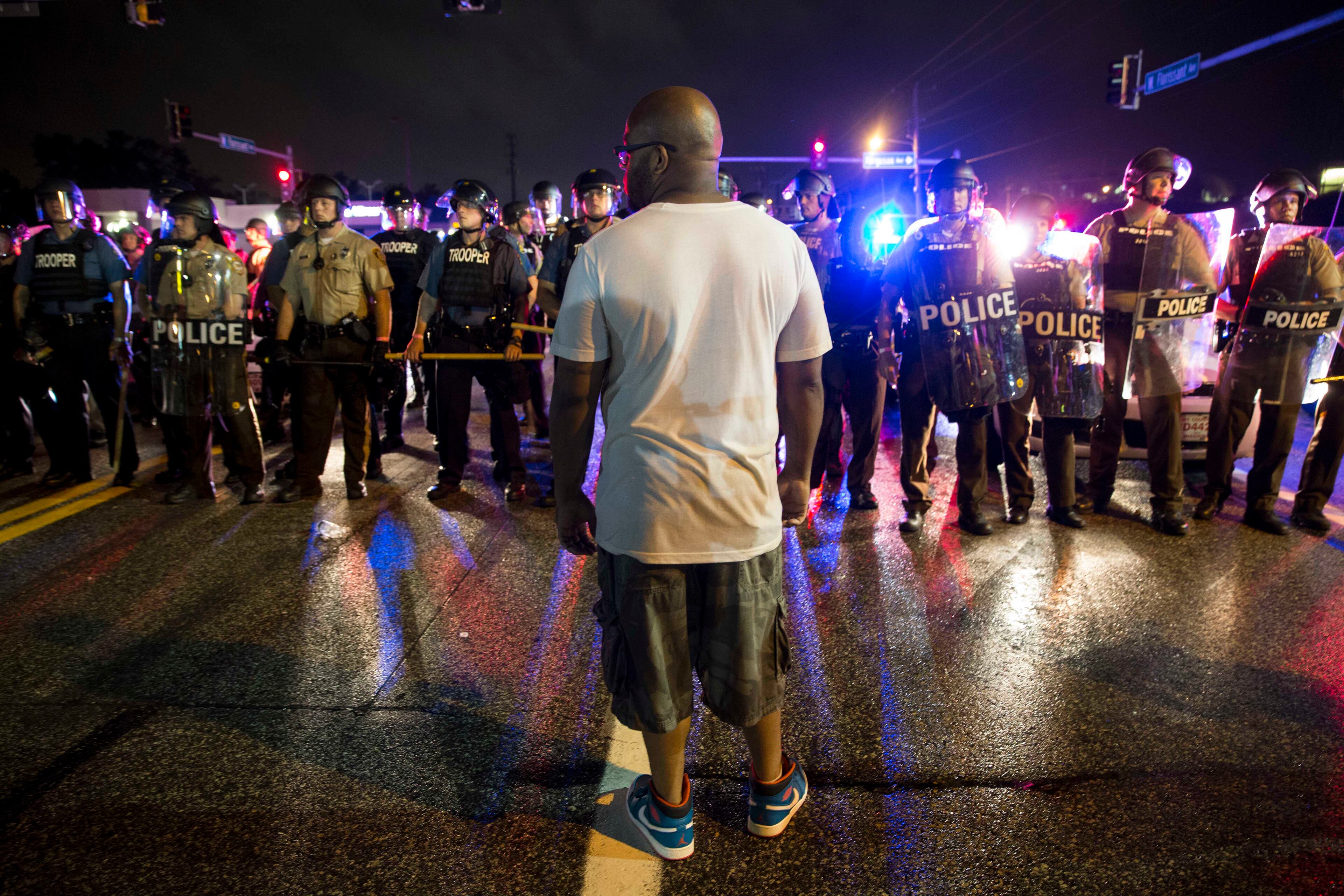 Police officers face off with protesters on West Florissant Avenue on the anniversary of Michael Brown's death in Ferguson, Mo., Aug. 9, 2015. A day of peaceful protest commemorating the killing of an unarmed black teenager by a white police officer one year ago ended in gunfire late Sunday. A St. Louis County police officer was involved in the shooting, the department said. (Whitney Curtis/The New York Times)