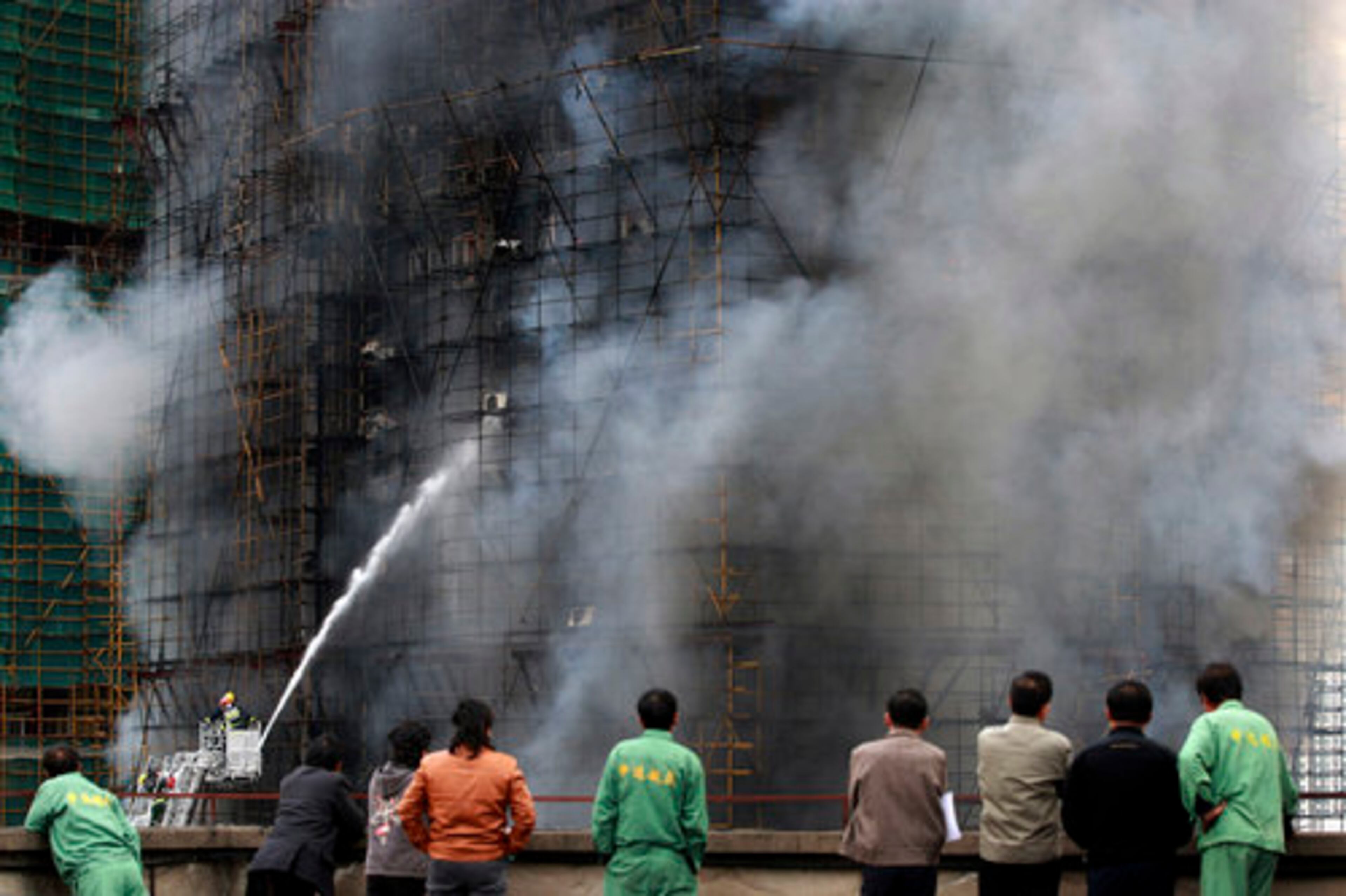 People from another building watch firefighters extinguish fire on an apartment building in the downtown area of Shanghai, east China, on Monday Nov. 15, 2010.