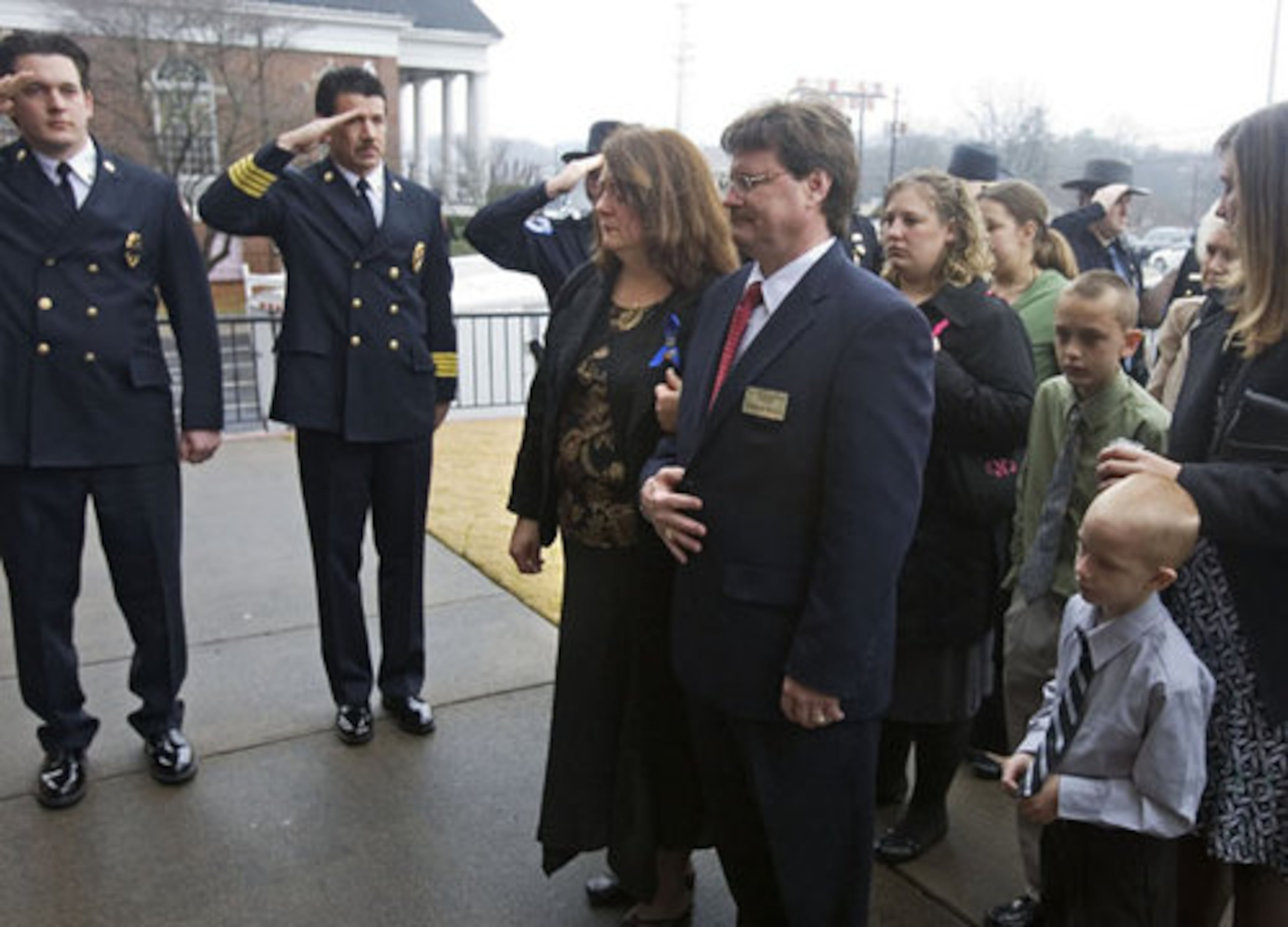 Public safety officers salute as Freddie Norman's widow, Faith Norman, and other family members, escorted by David Roach from the West Cobb Funeral Home, follow a Cobb County Police honor guard carrying Norman's casket into the church for the funeral.