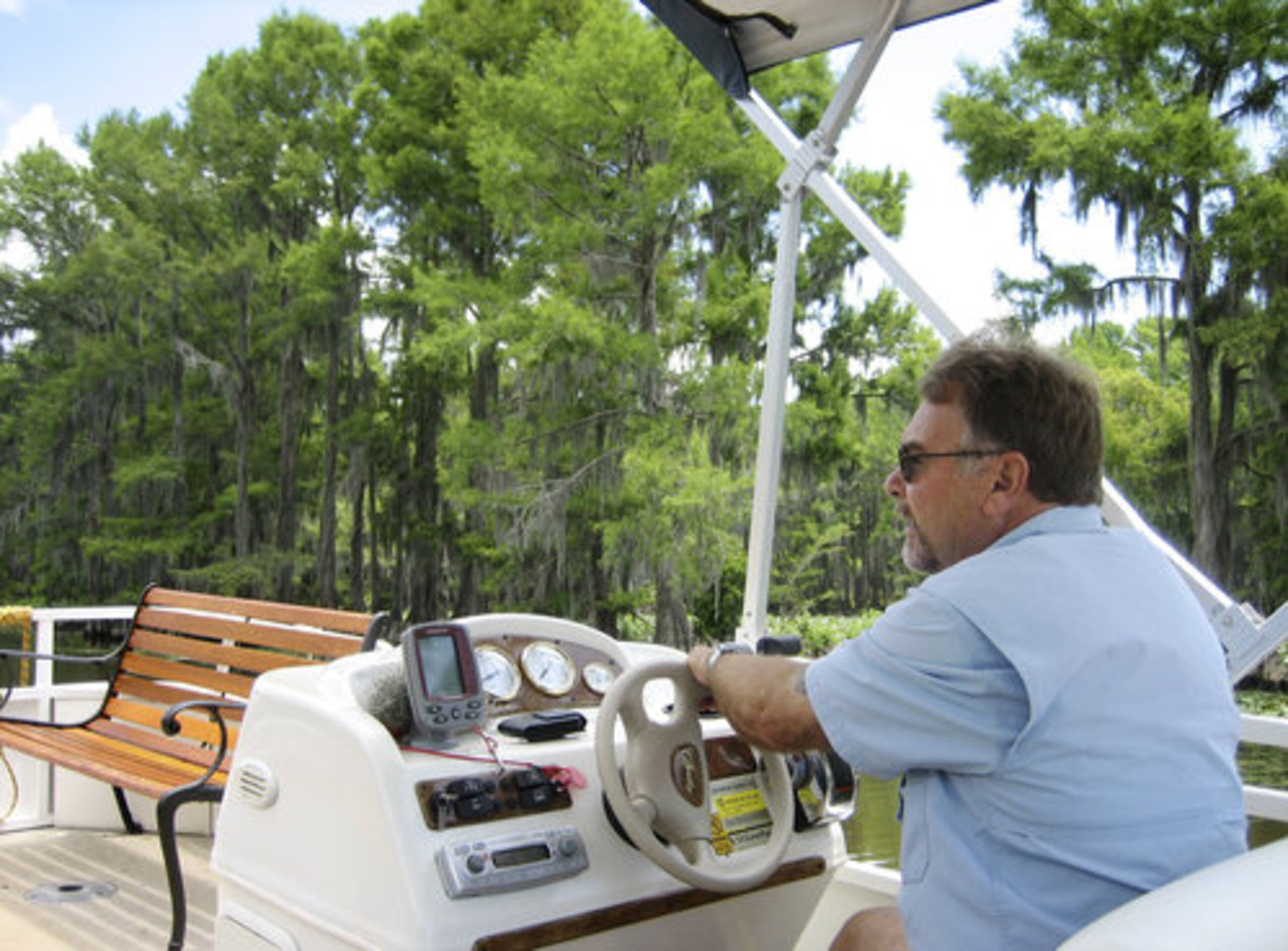 Boat Capt. Ron Gibbs navigates his pontoon along a tree line on Caddo Lake during a tour near Uncertain, Texas. A boat tour of the lake takes visitors through seas of bright green water lilies, down shaded watery avenues and past islands of dense forest.