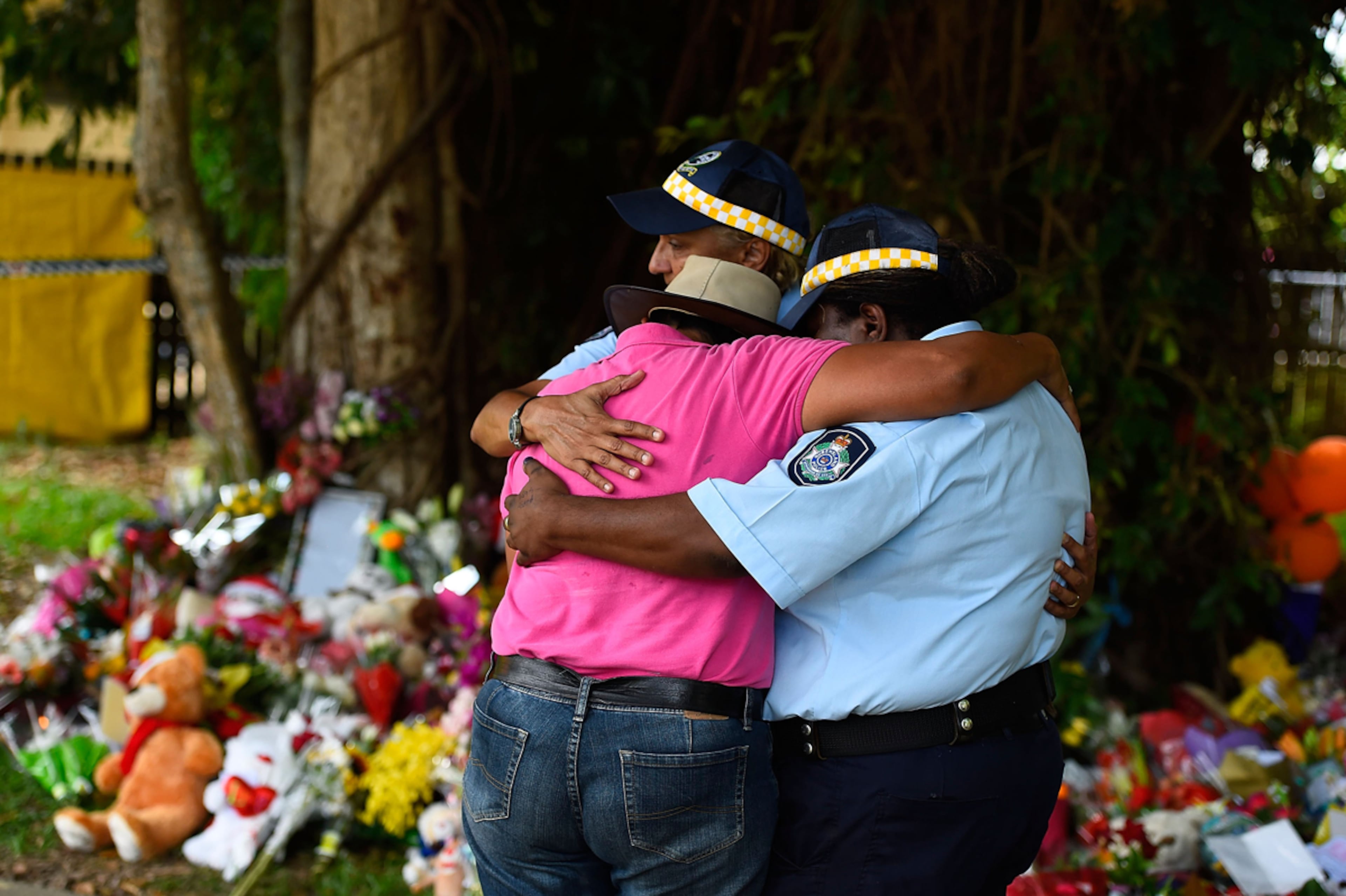 STABBING MEMORIAL--CAIRNS, AUSTRALIA - DECEMBER 20: Mourners embrace next to a memorial in the park next the home of a multiple stabbing in the suburb of Manoora on December 20, 2014 in Cairns, Australia. Eight children have been found dead and a 37-year-old woman is in hospital with chest injuries at a home in North Queensland. The children, aged 18 months to 14 years have reportedly been stabbed and the women has been arrested for murder. (Photo by Ian Hitchcock/Getty Images) *** BESTPIX ***