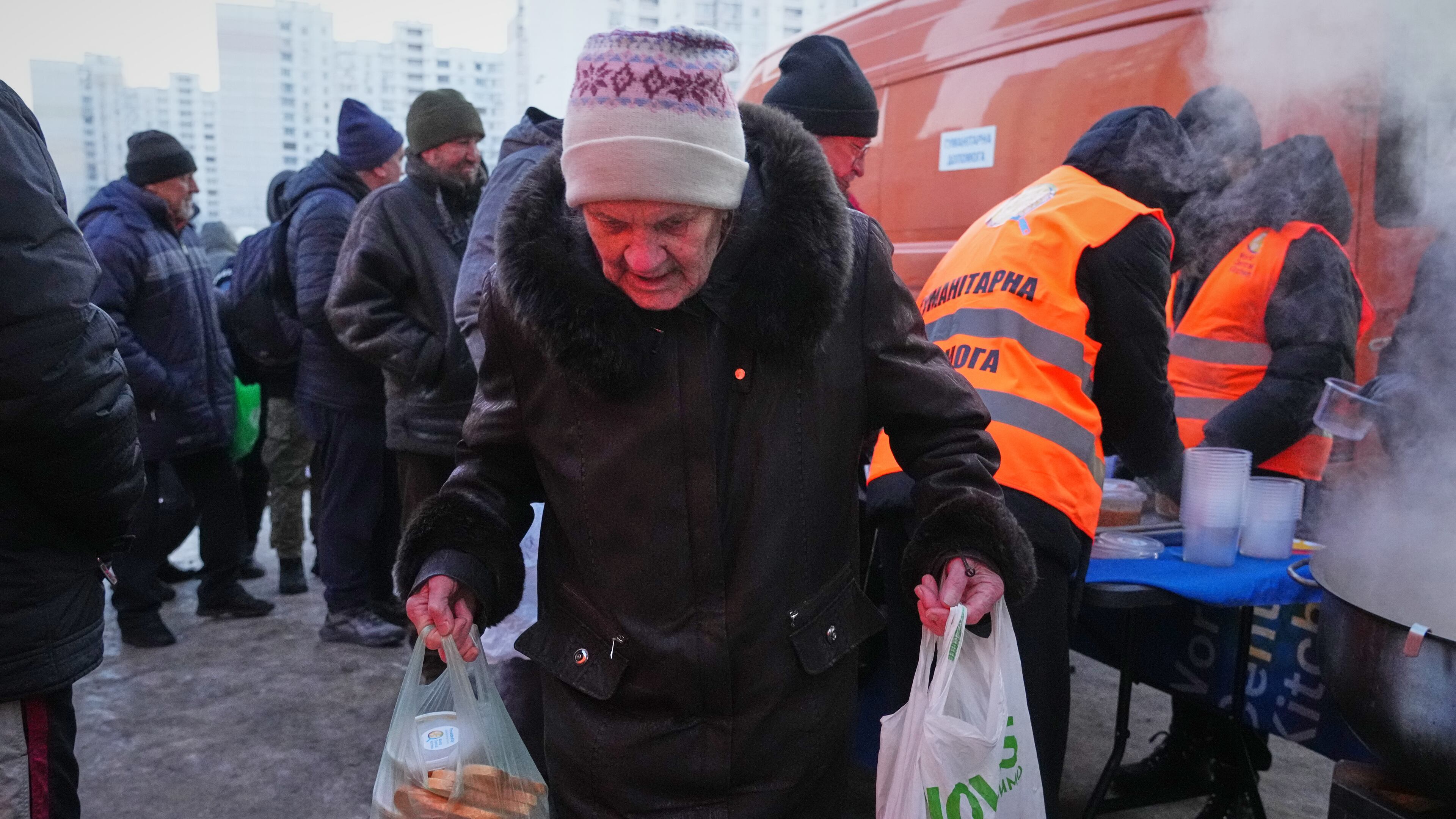 An elderly woman carries her bags out of a hot food distribution point during a power outage caused by Russia's repeated air strikes on the country's power grid, in Kyiv, Ukraine, Monday, Feb. 2, 2026. (AP Photo/Sergey Grits)