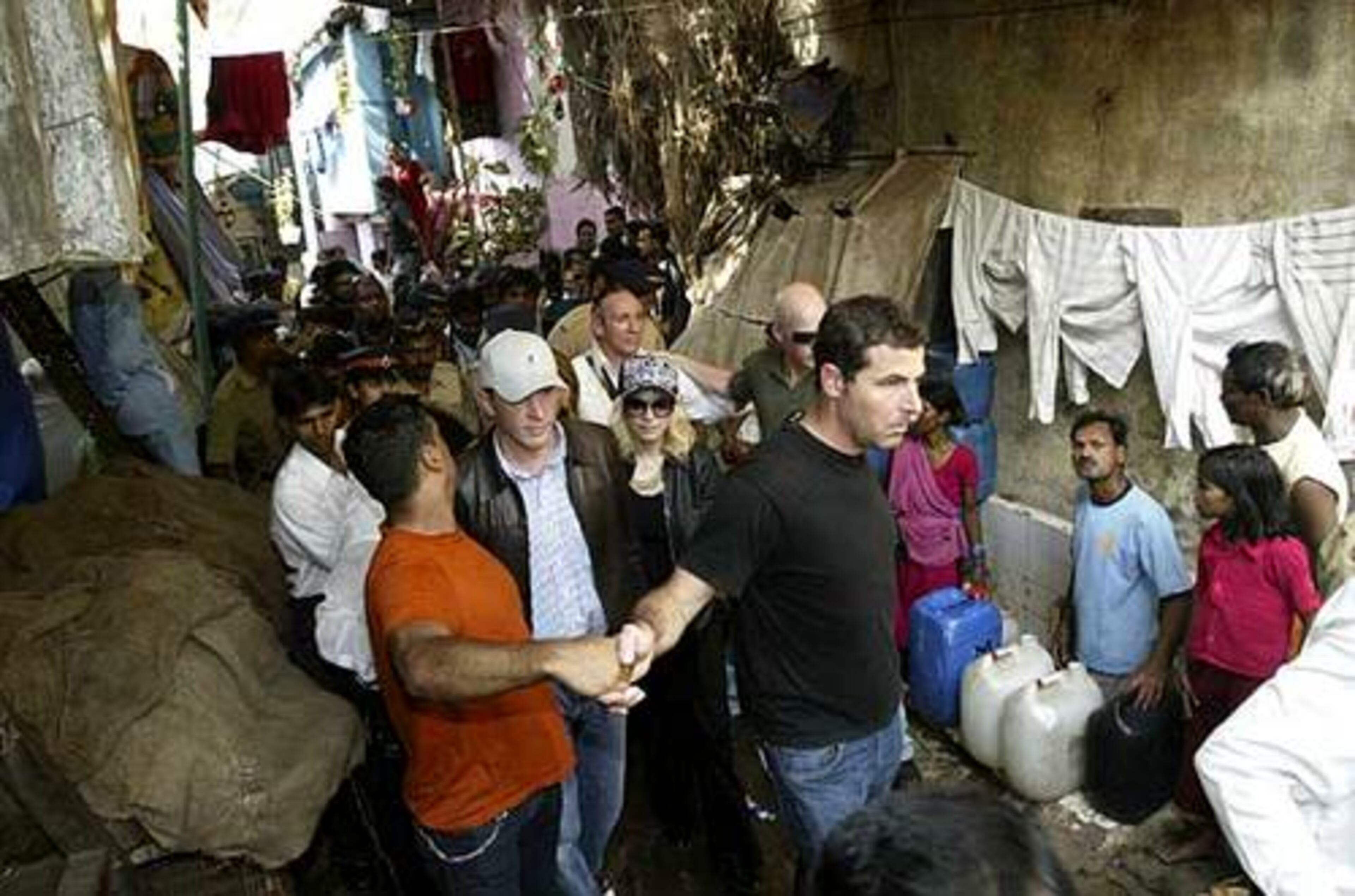 The hand-holding security guys are a veritable conga line by the time they brush past the hanging laundry in the shanty town.