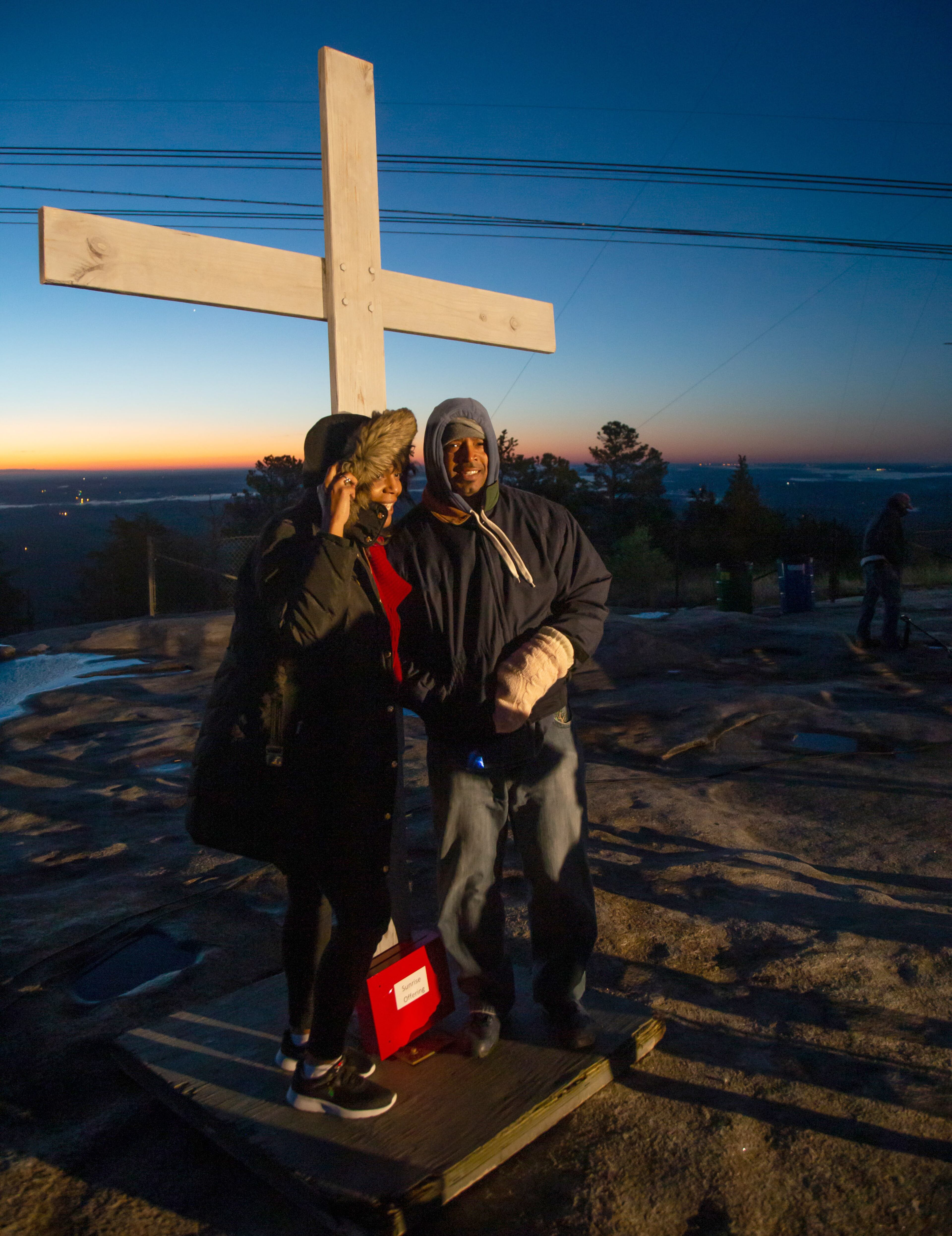 Amy Rankine and Mario Dabney pose for a photograph with the large cross on top of Stone Mountain before the start of the 75th Annual Easter Sunrise Service on Sunday, April 21, 2019. STEVE SCHAEFER / SPECIAL TO THE AJC