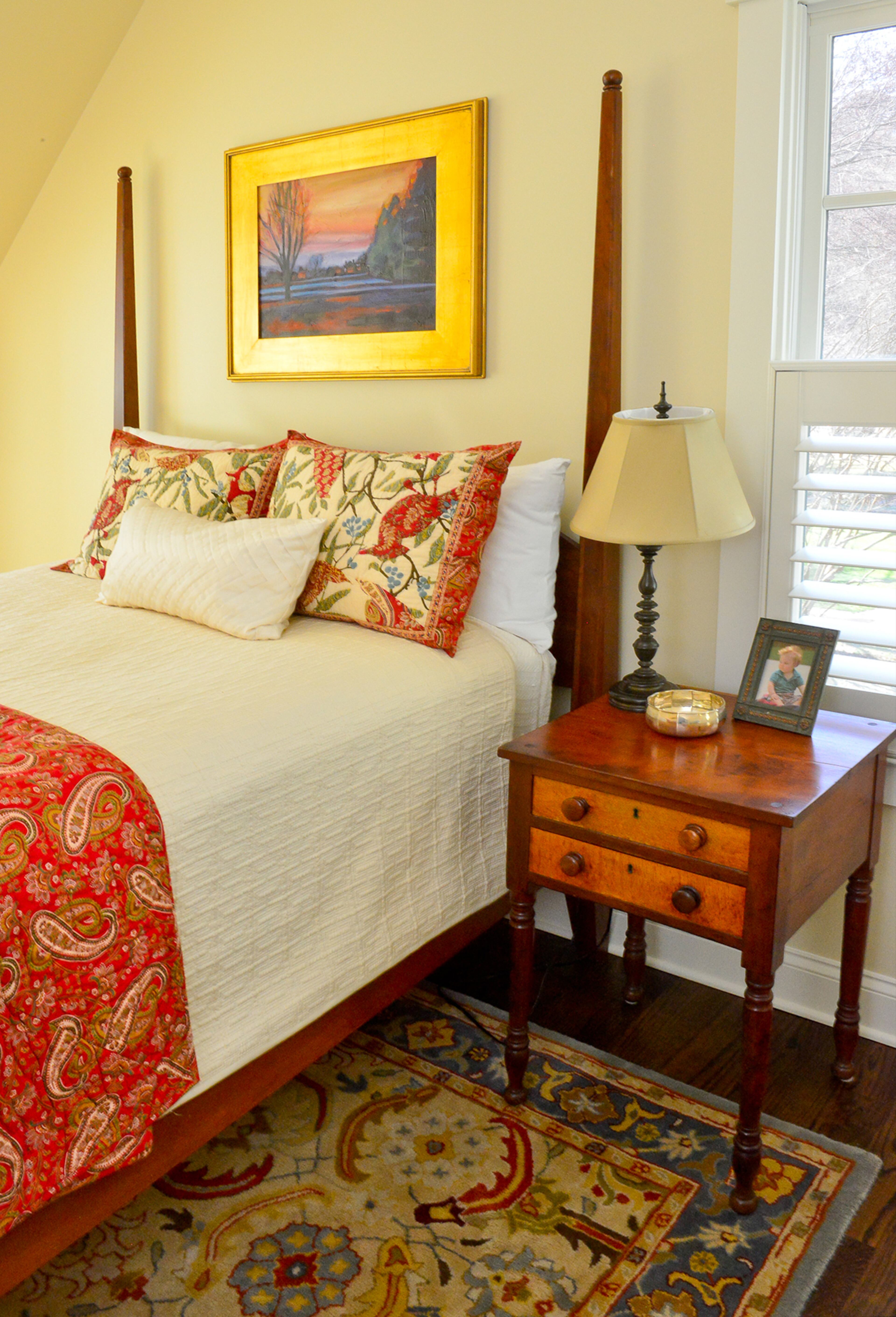 In the upstairs guest bedroom, an Ethan Allen bed with Pottery Barn bedding complements a family heirloom side table. Paintings in the room are by Keith Spencer.