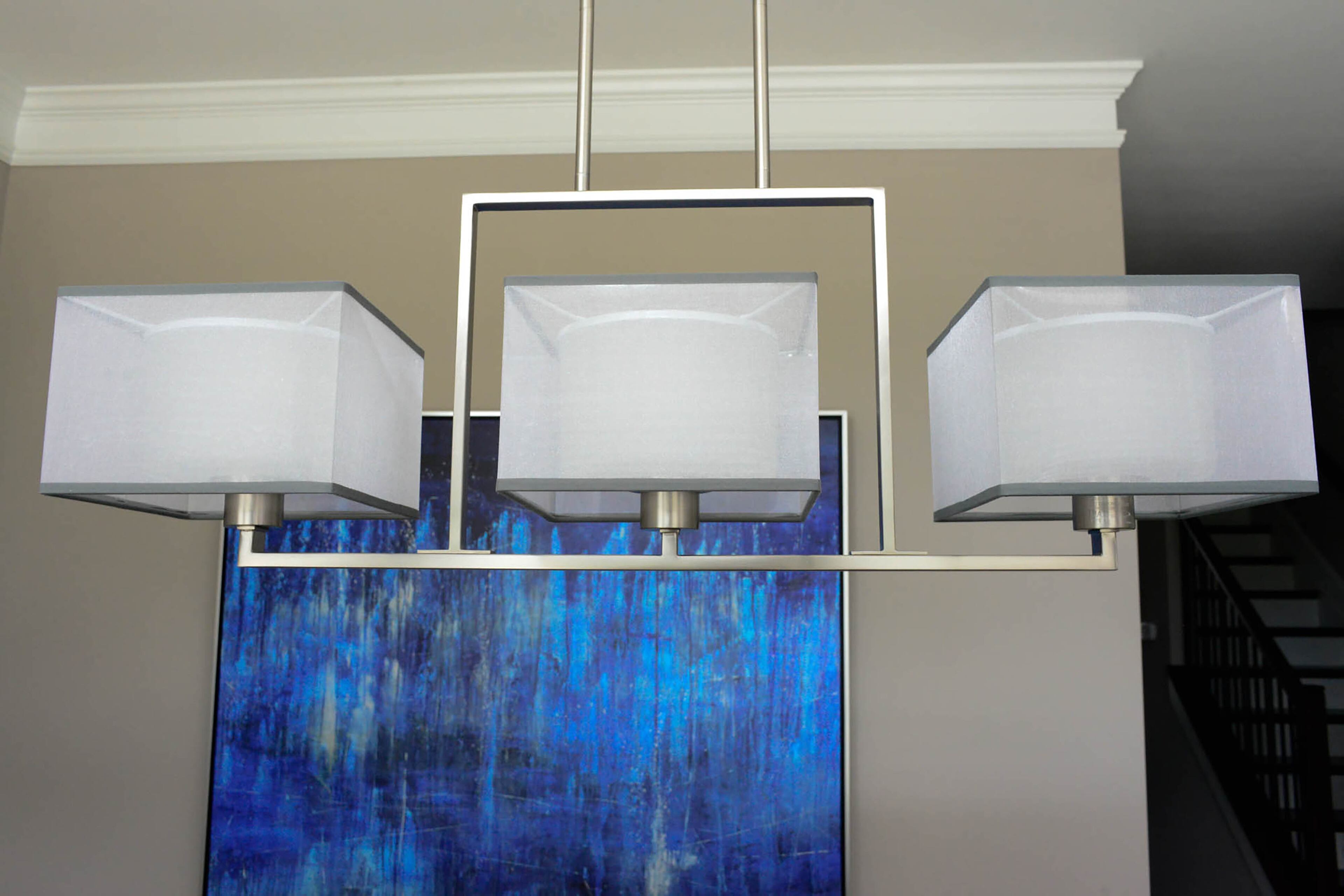 The homeowner accentuates his modern style with this Kailey 3 Light Linear Chandelier in brushed nickel by Kichler Lighting. The organza cubic shades soften both the light and overall tone of the piece. The striking blue in the artwork behind it, from GreatBigCanvas.com, gives the dining room a pop of color.