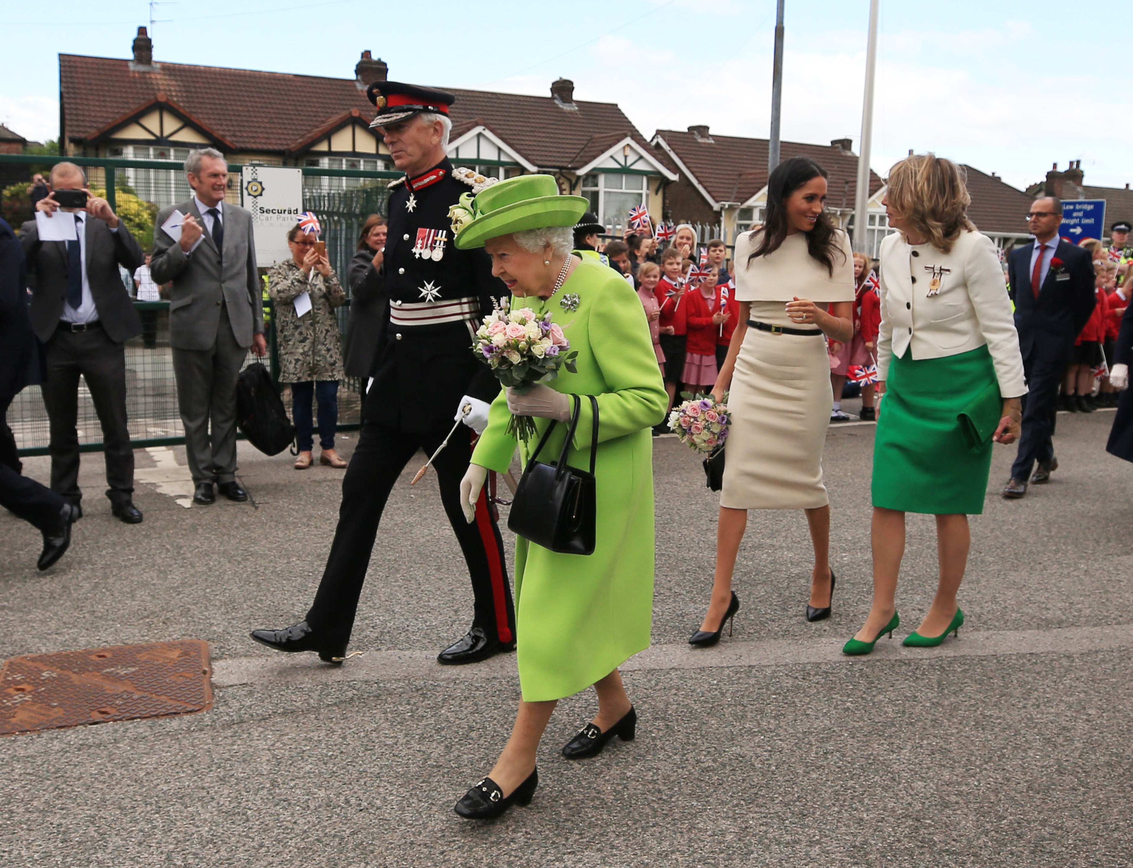 RUNCORN, CHESHIRE, ENGLAND - JUNE 14: Queen Elizabeth II holds flowers as she and Meghan, Duchess of Sussex greet the crowds after arriving by Royal Train at Runcorn Station to open the new Mersey Gateway Bridge on June 14, 2018 in the town of Runcorn, Cheshire, England. Meghan Markle married Prince Harry last month to become The Duchess of Sussex and this is her first engagement with the Queen. During the visit the pair will open a road bridge in Widnes and visit The Storyhouse and Town Hall in Chester. (Photo by Peter Byrne - WPA Pool/Getty Images)